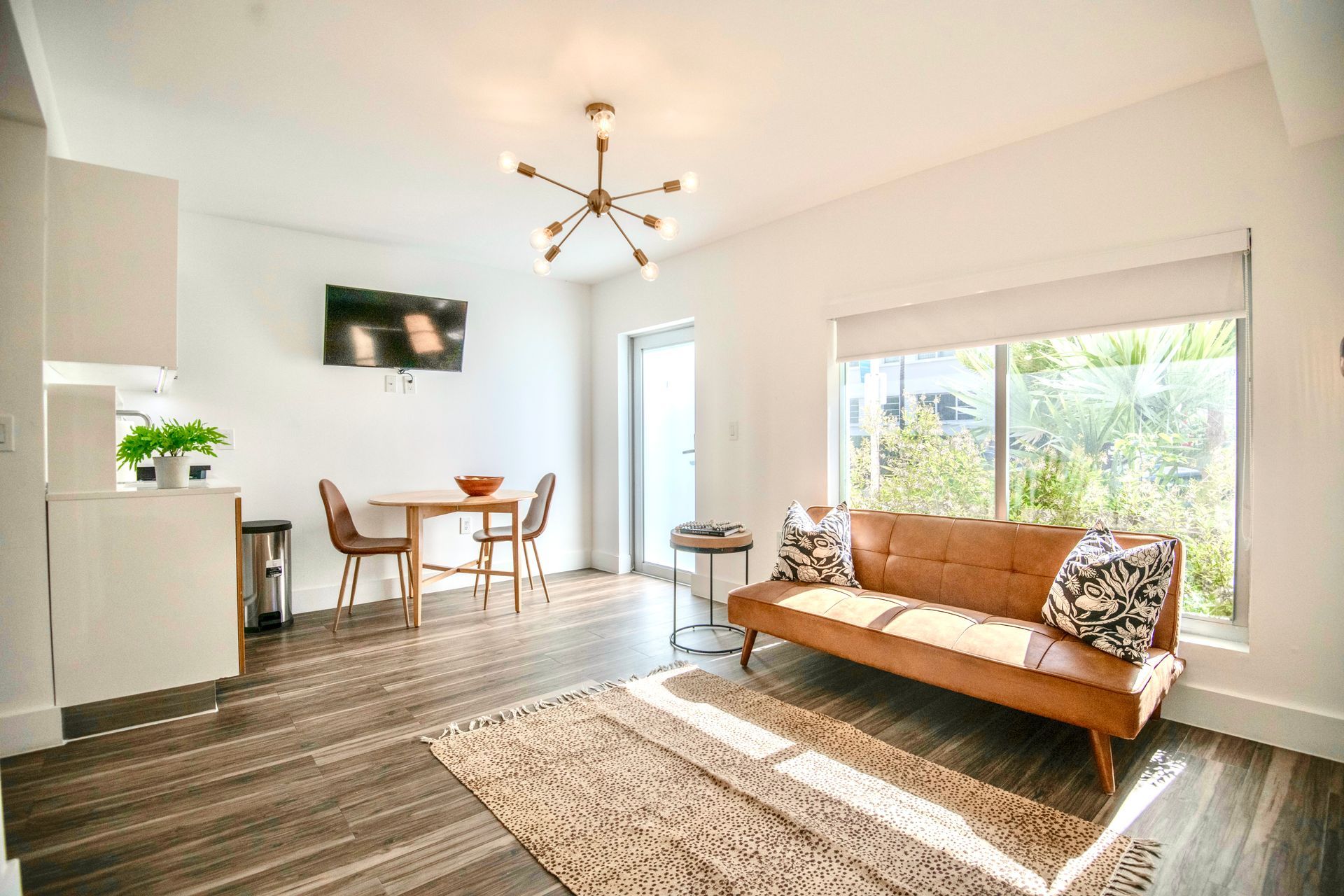 Modern living space with brown sofa, small dining area, and large window with sunlight.