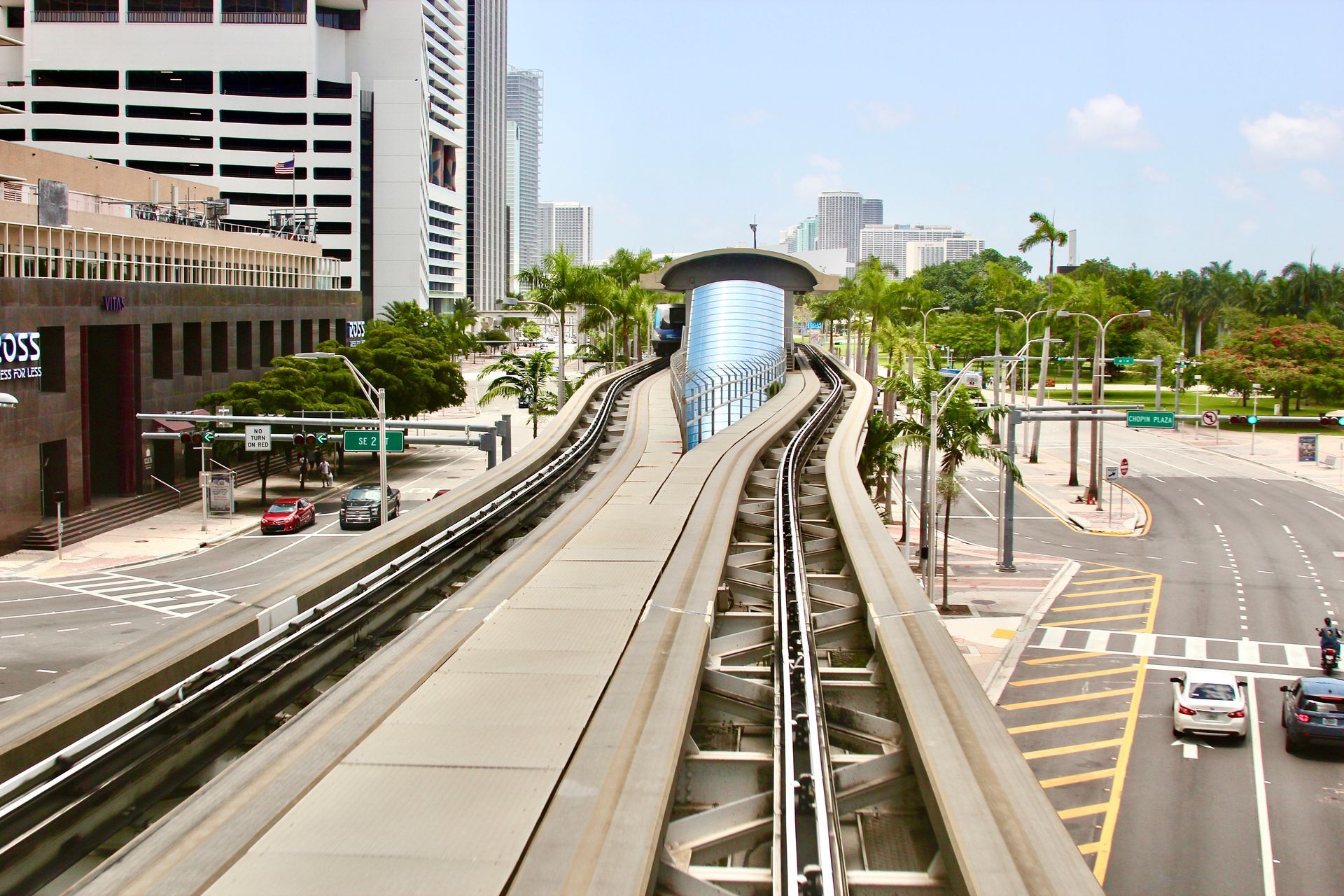 Elevated monorail track in Miami, Florida. Cars, buildings, palm trees, and sunny sky are visible.