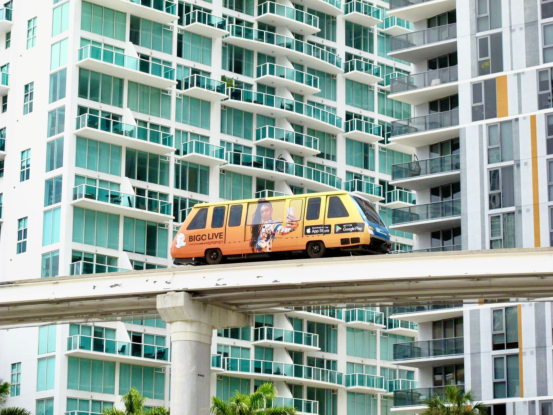 Monorail car traveling on elevated track in front of a high-rise building with light blue balconies.
