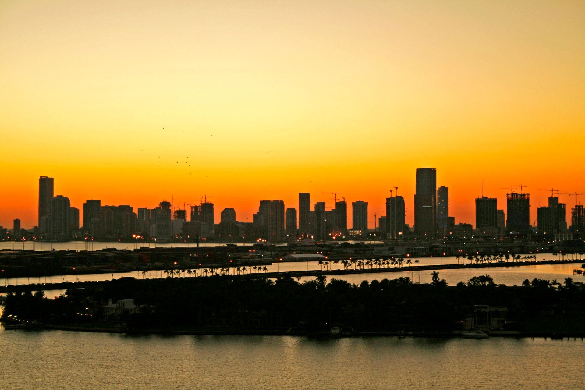 Silhouette of a city skyline against an orange and yellow sunset over the water.