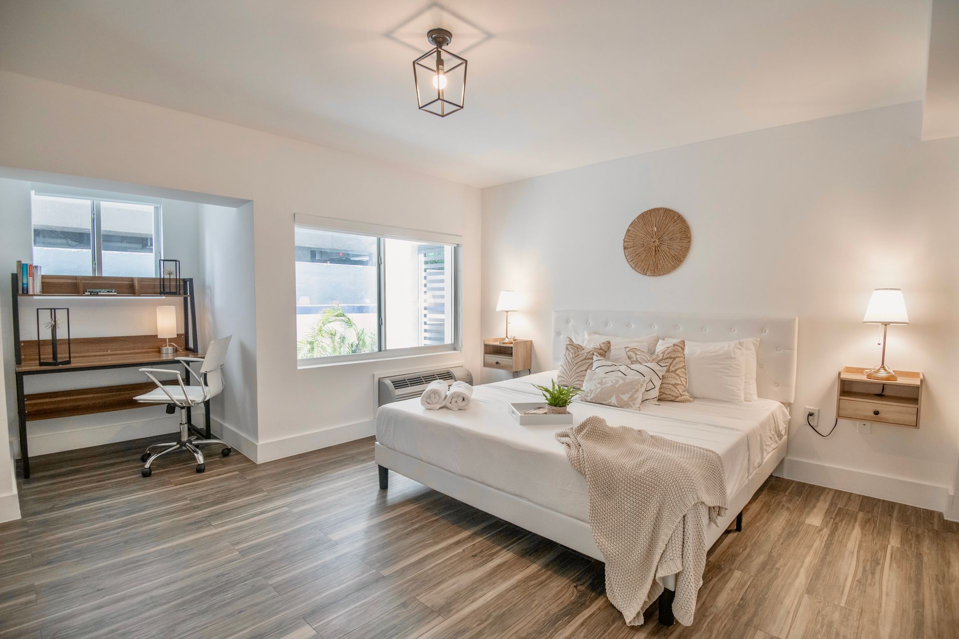 Bedroom with a white bed, desk, and window, light wood floors, and neutral decor.