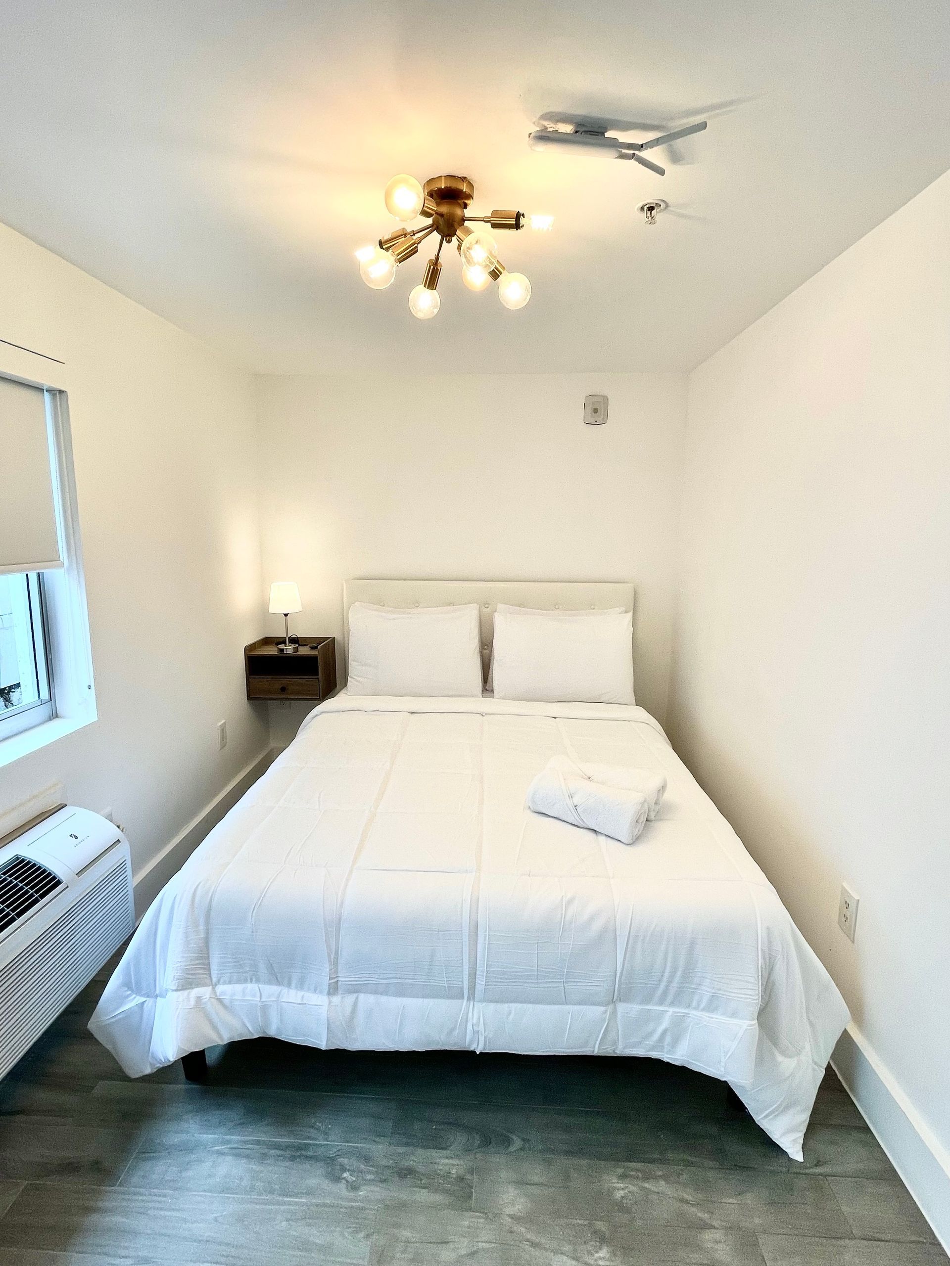 Small white bedroom with a bed, a nightstand, and a Sputnik-style light fixture.