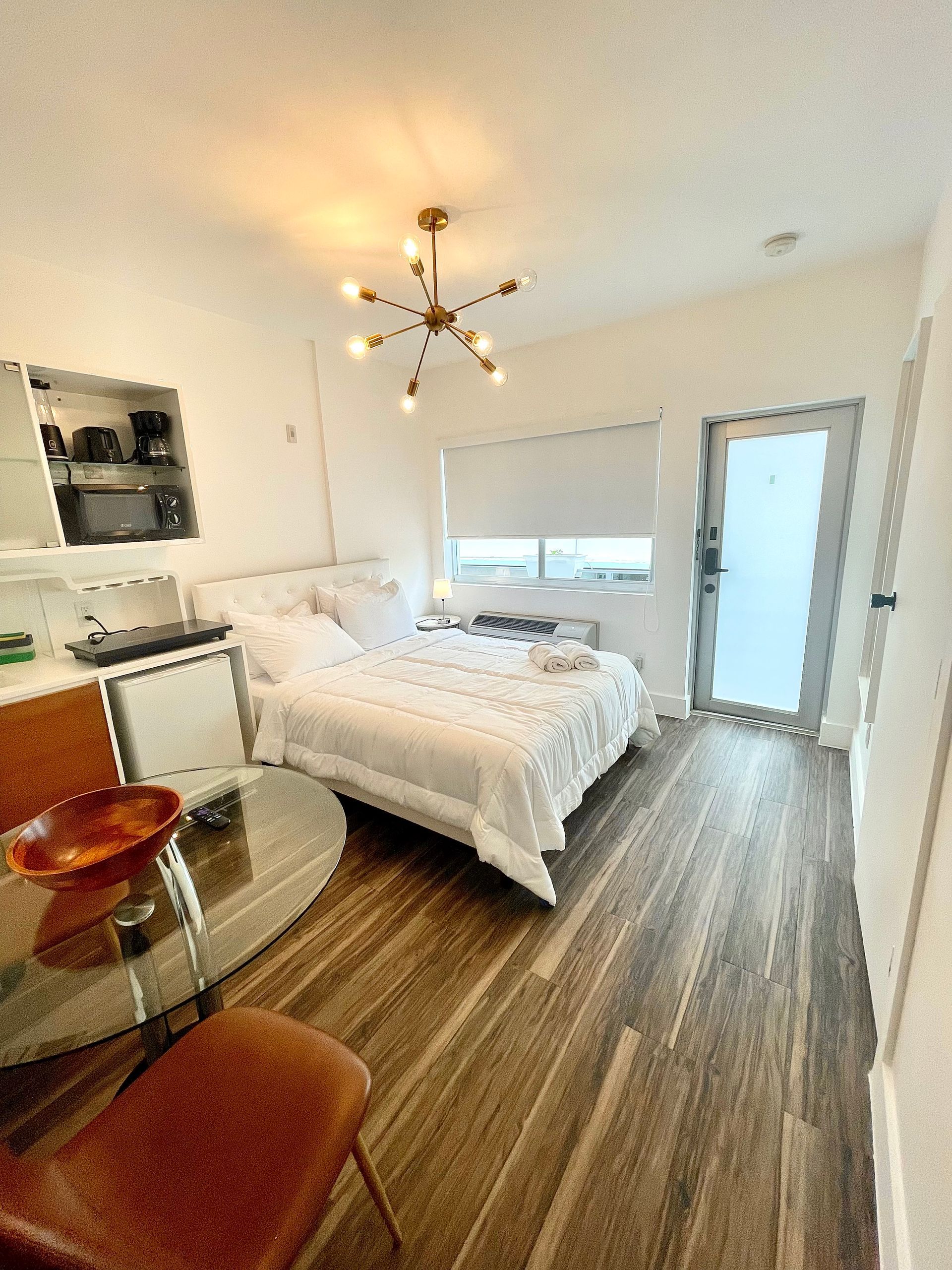Small studio apartment with bed, small table, and wooden floors.