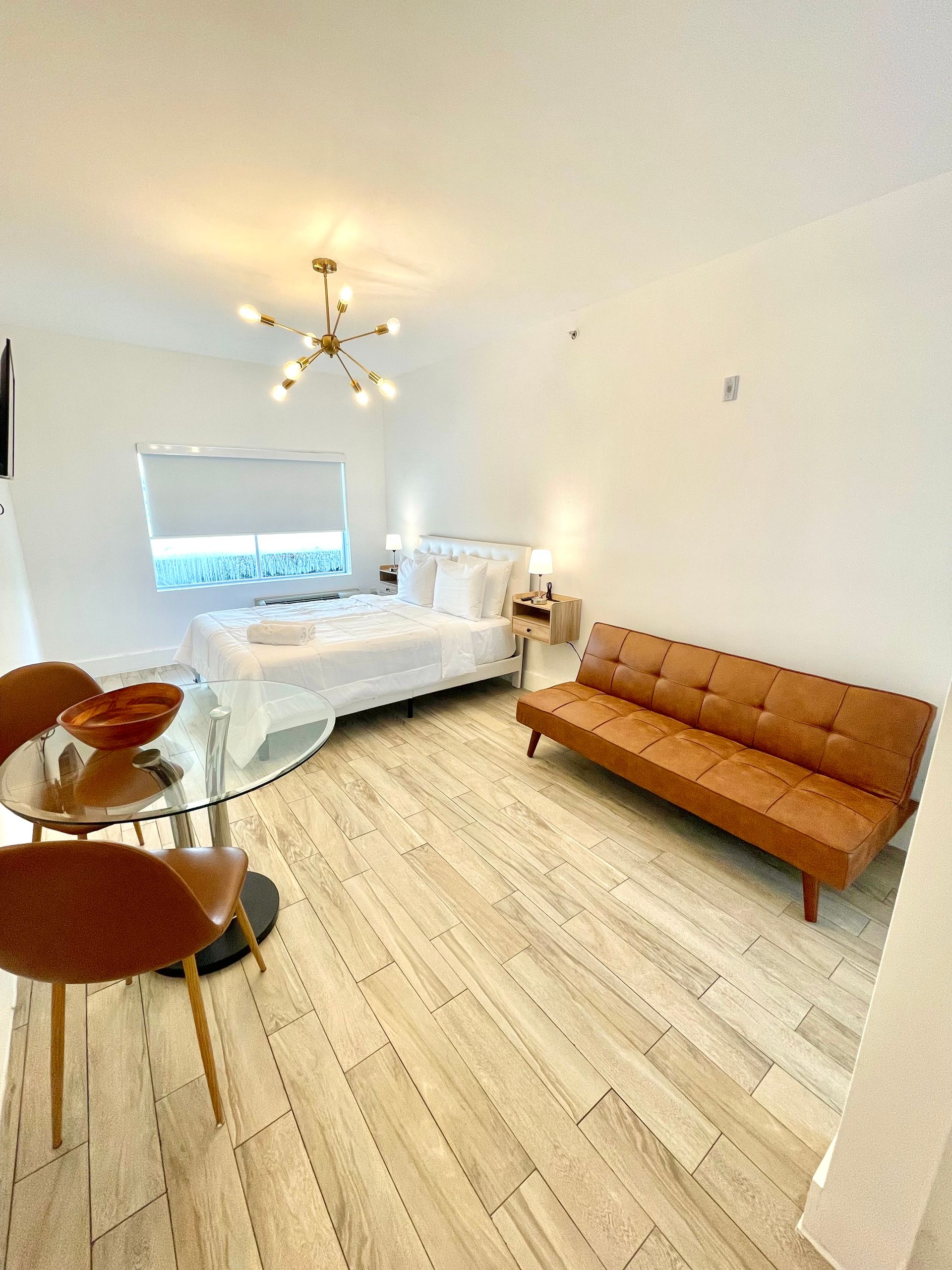 Modern studio apartment with light wood floors, a bed, sofa, and glass-top dining table.