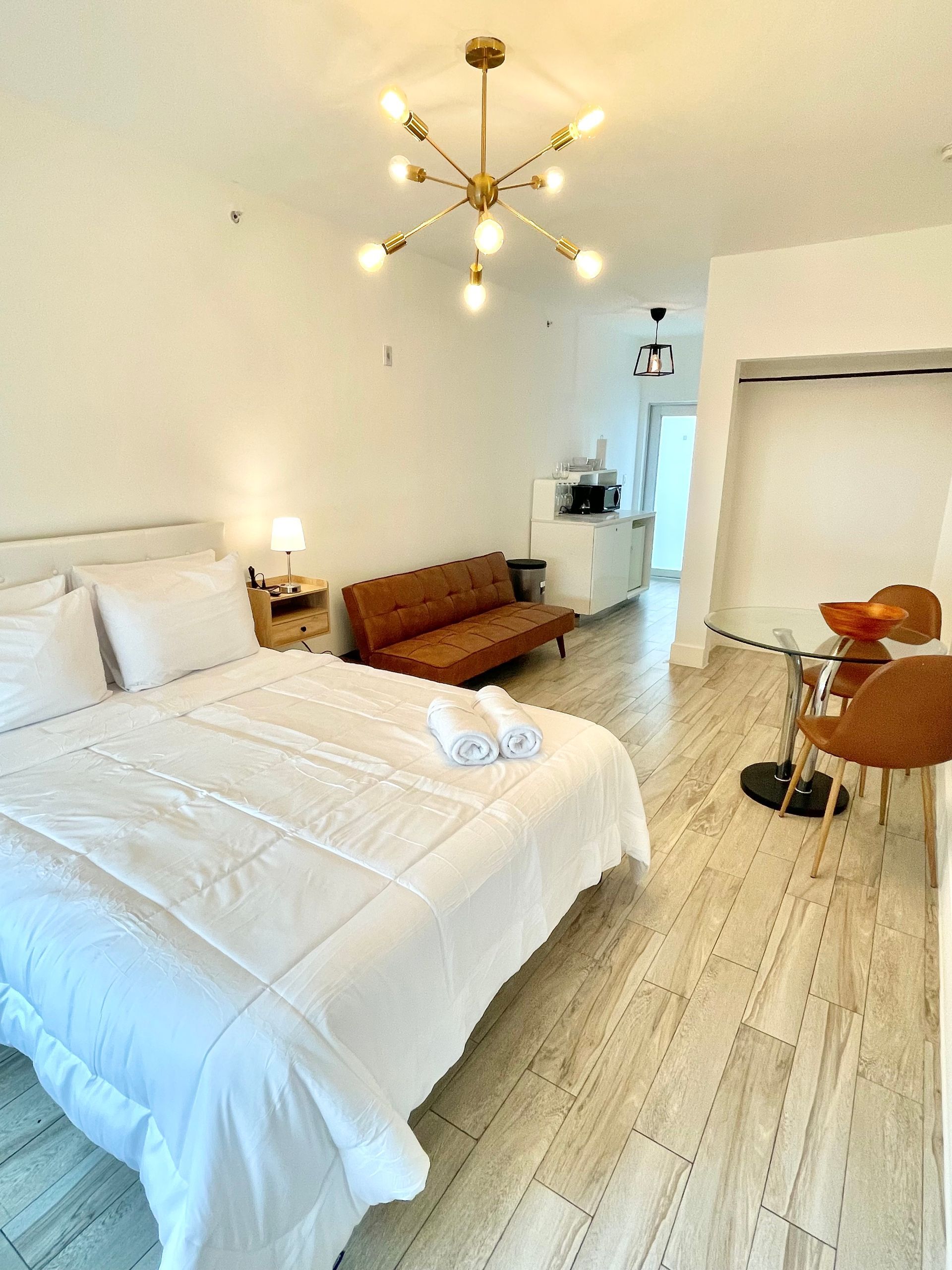 Cozy studio apartment with a bed, sofa, small dining area, and kitchenette. White walls, light wood floors.
