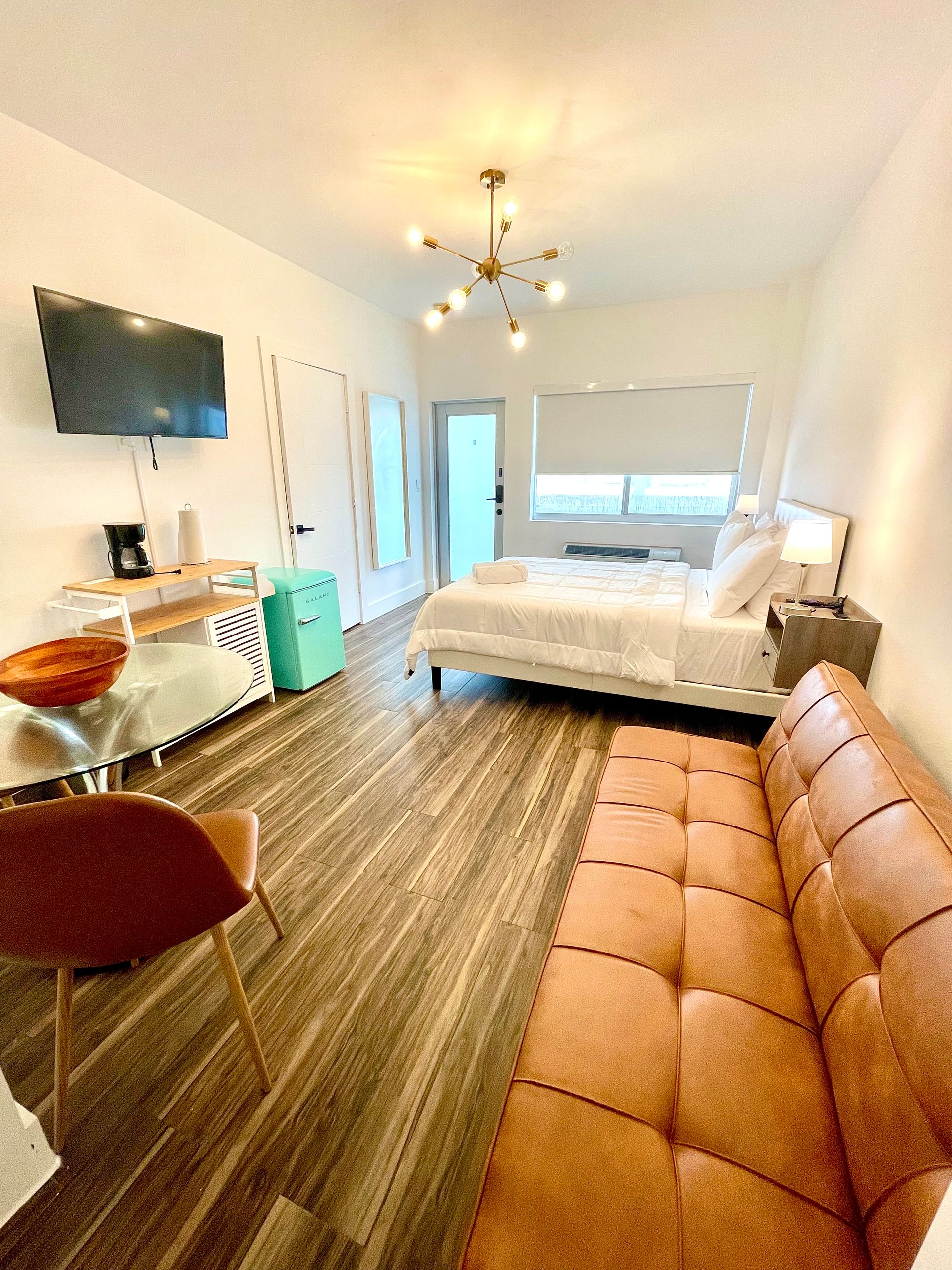 Studio apartment with bed, sofa, and TV; light wood floors.
