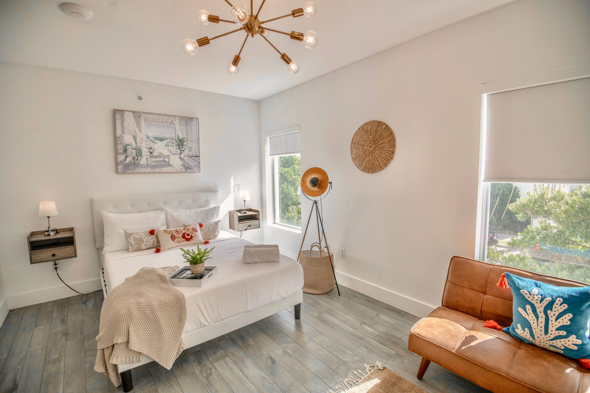 Bedroom with a white bed, wooden accents, and a brown leather couch. Bright and airy.
