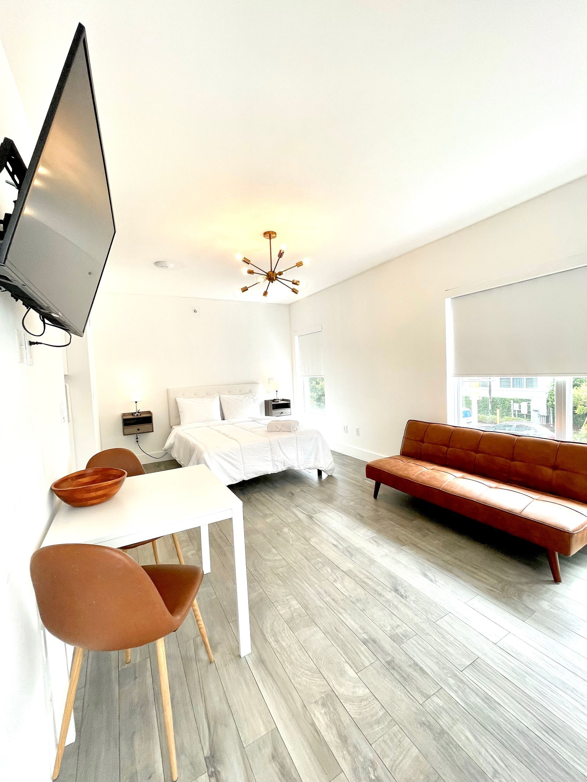 Bright studio apartment with a bed, small table, and brown sofa.