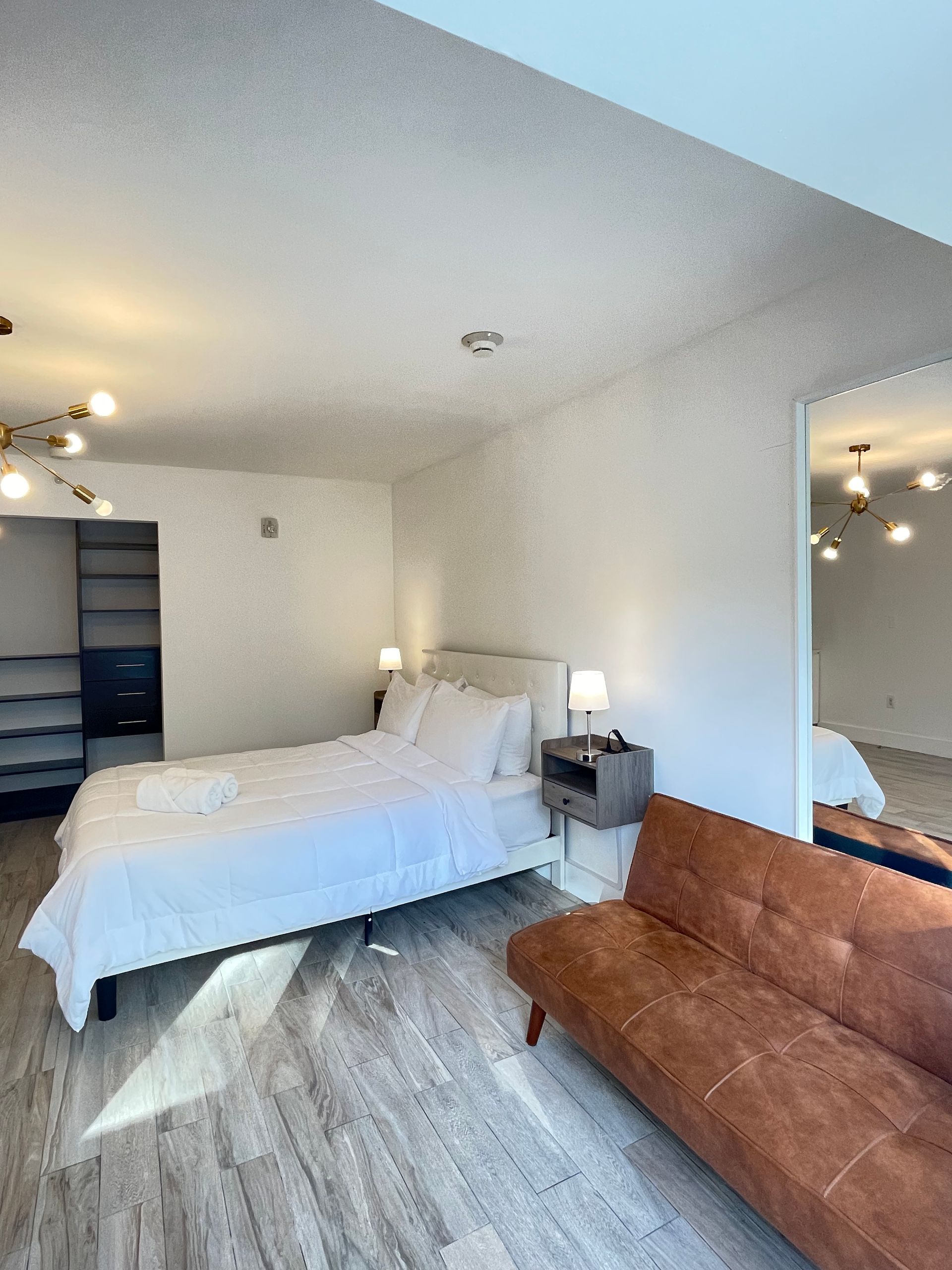 White bedroom with bed, sofa, and wardrobe. Wooden floors and a large mirror.