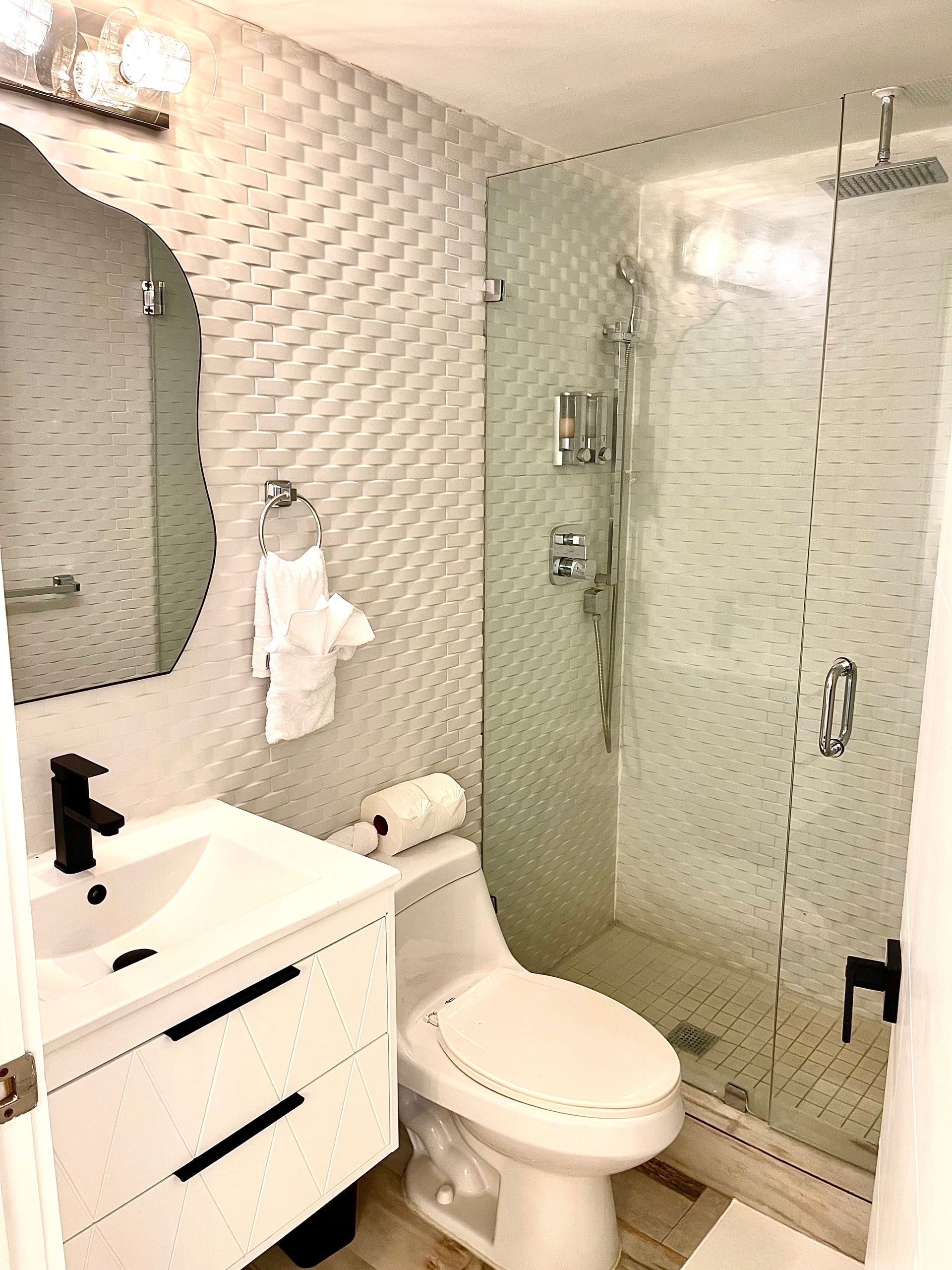 Modern white bathroom with shower, toilet, and vanity; decorative tiled wall.