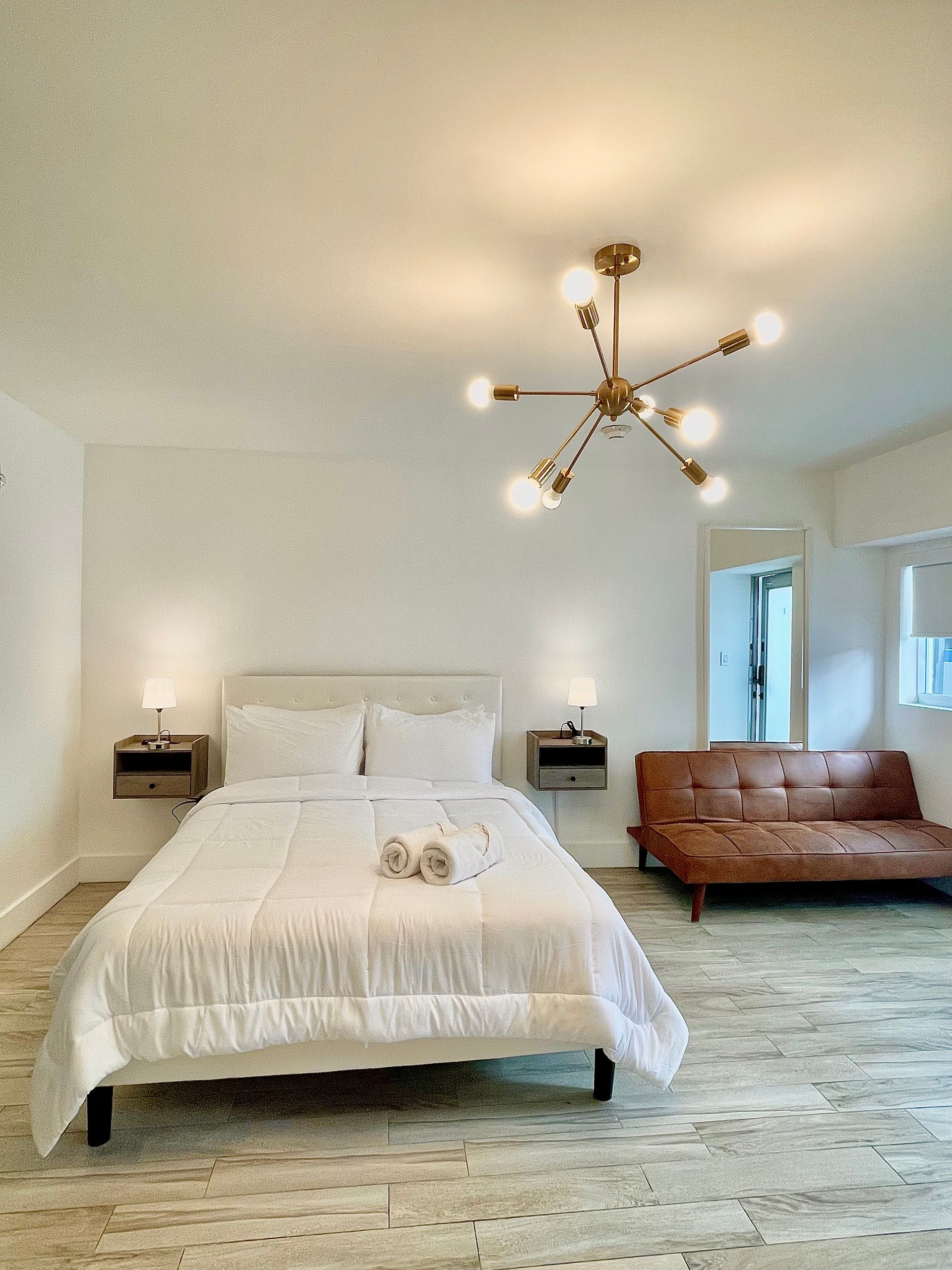 Bedroom with a bed, futon, and modern light fixture; neutral colors.