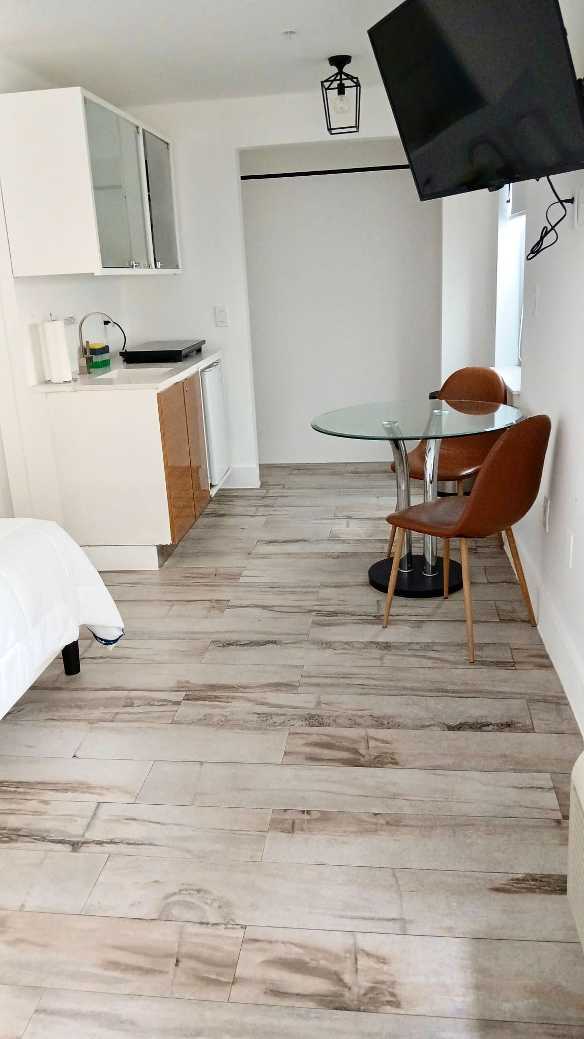 Small studio apartment with kitchen, dining area, and TV. Wooden floor.