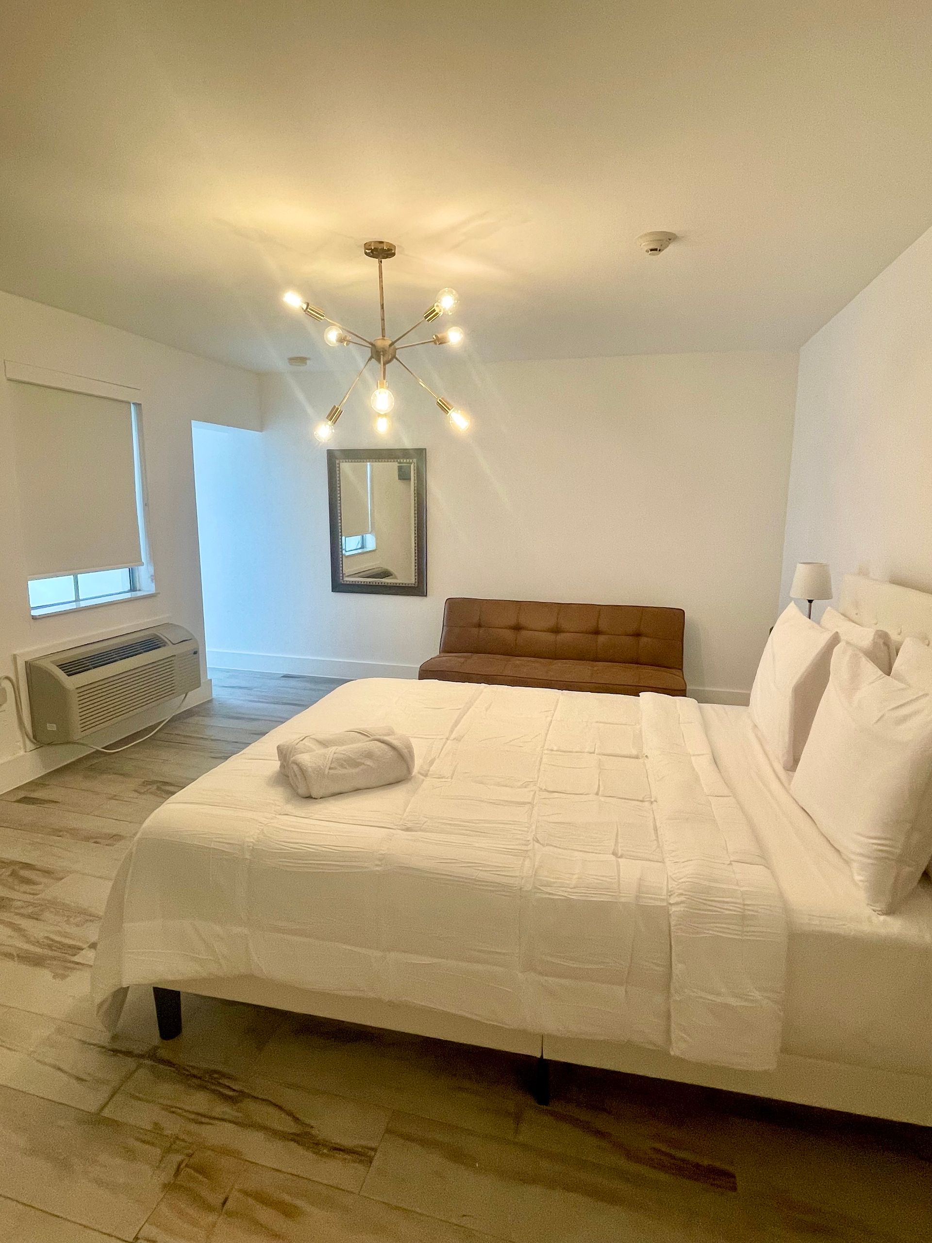 Bright bedroom with white bedding, a brown sofa, and a decorative light fixture.