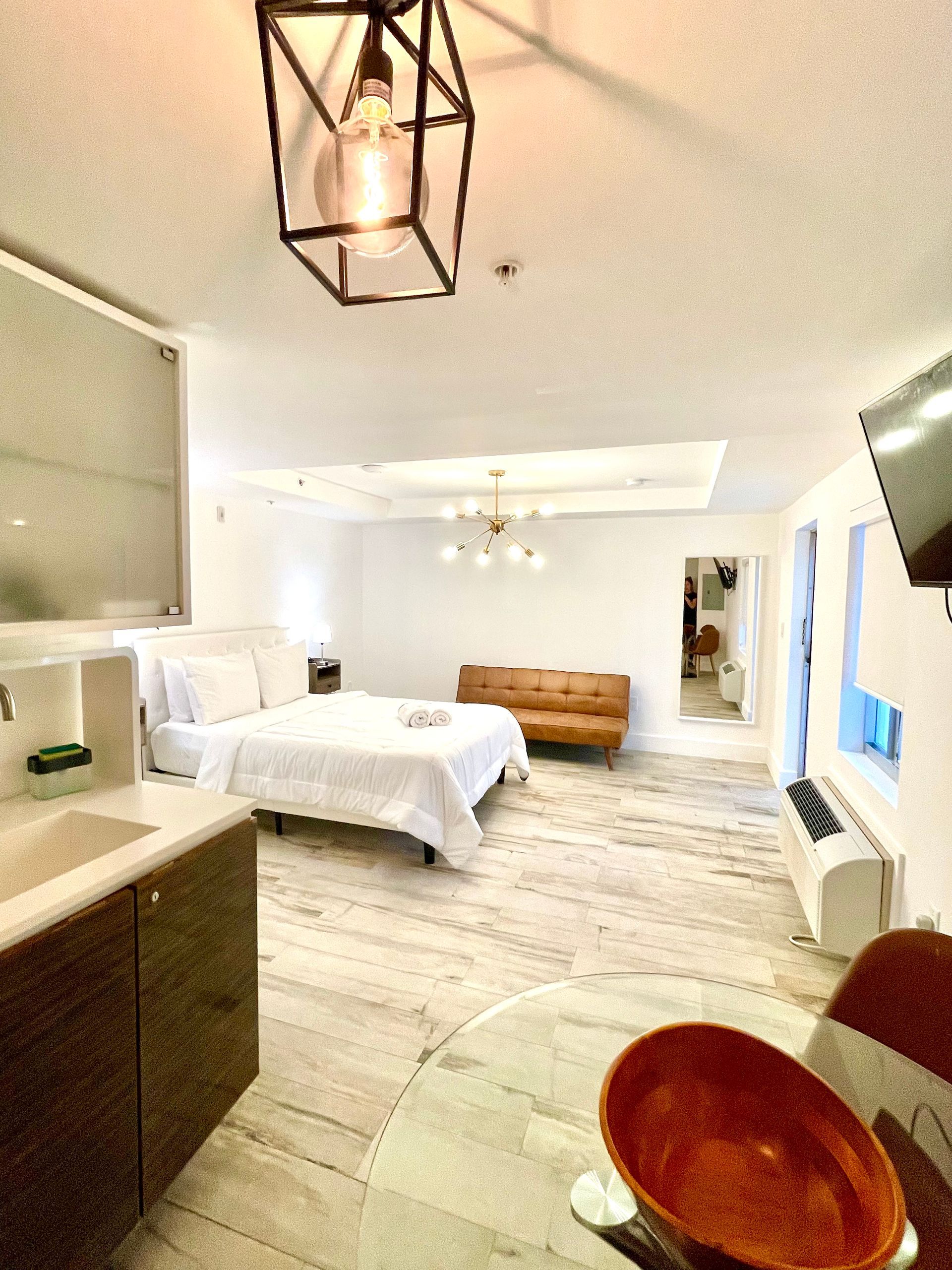 Modern studio apartment with bed, couch, and dining area. Light wood floors and bright, open space.