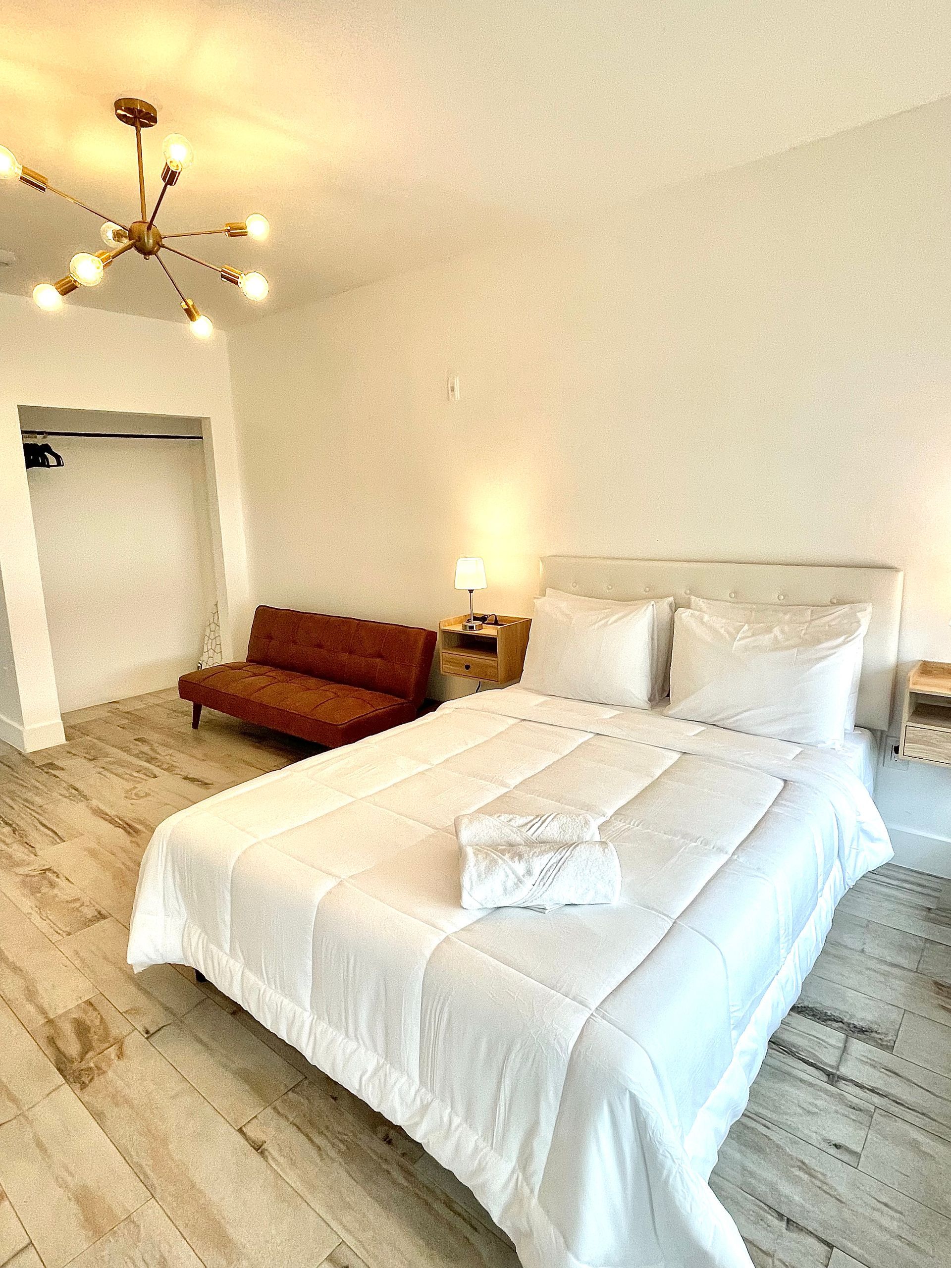 Bedroom with a white bed, brown couch, and a modern light fixture.