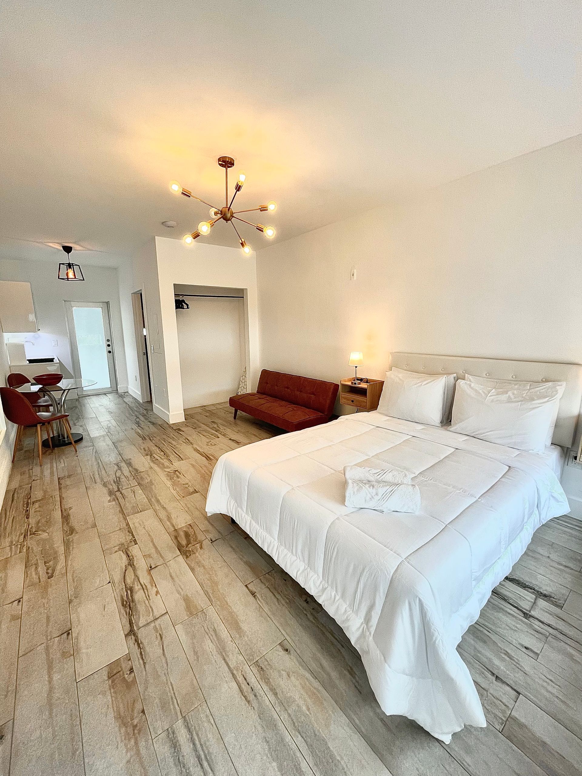 Bright studio apartment with a bed, red sofa, and wood-look flooring.