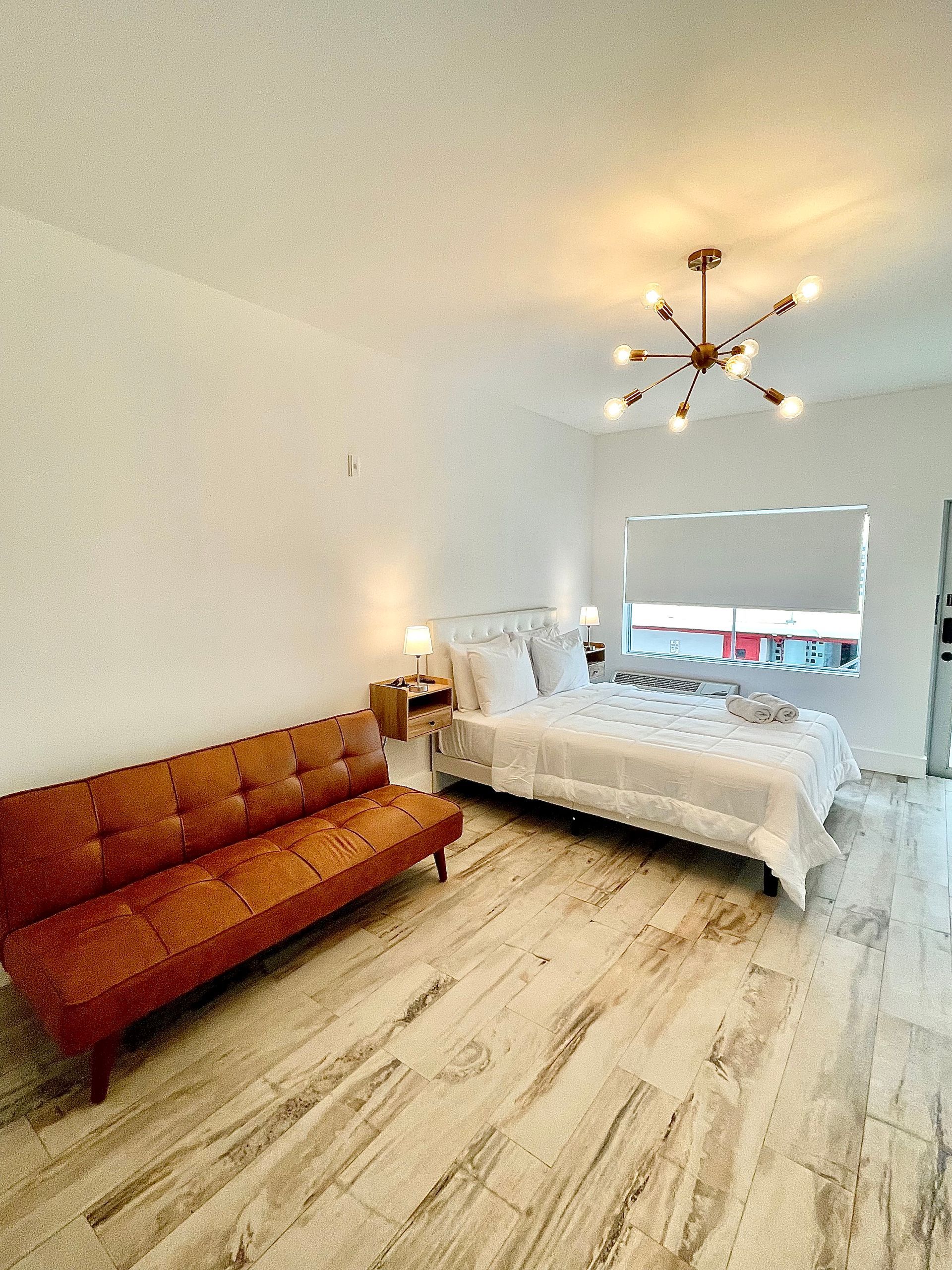 A bright bedroom with a bed, brown sofa, and a modern chandelier. Light marble floors.