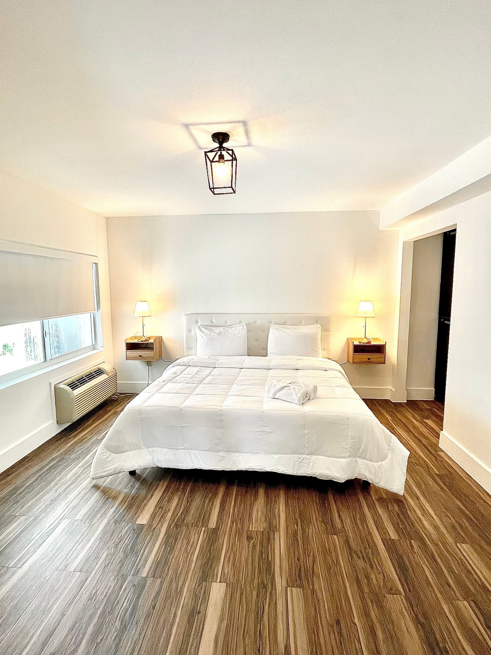 Bedroom with white bedding, wooden floor, bedside tables, and a window.