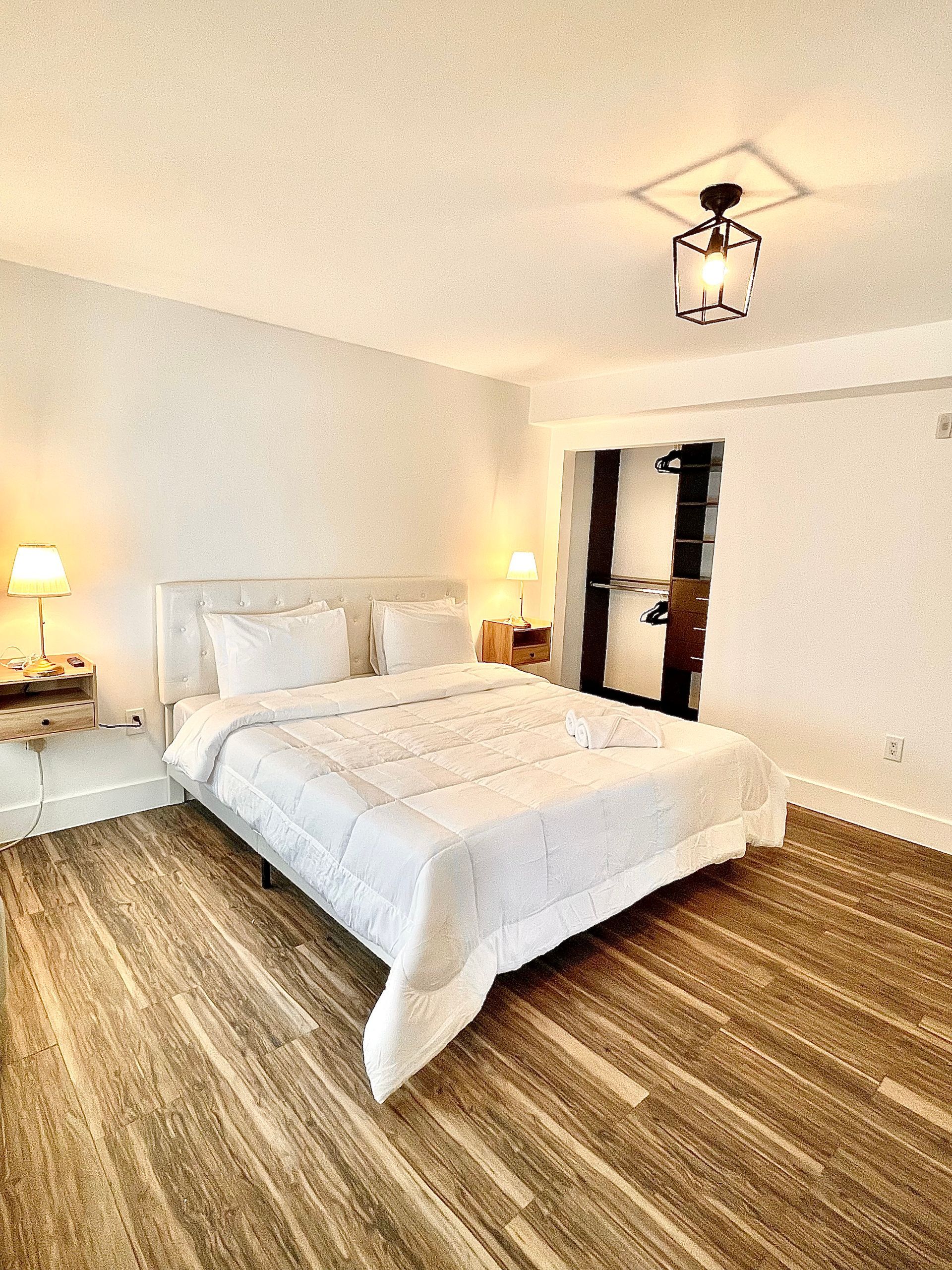 Bedroom with a white bed, wooden floor, white walls, bedside lamps, and a black light fixture.