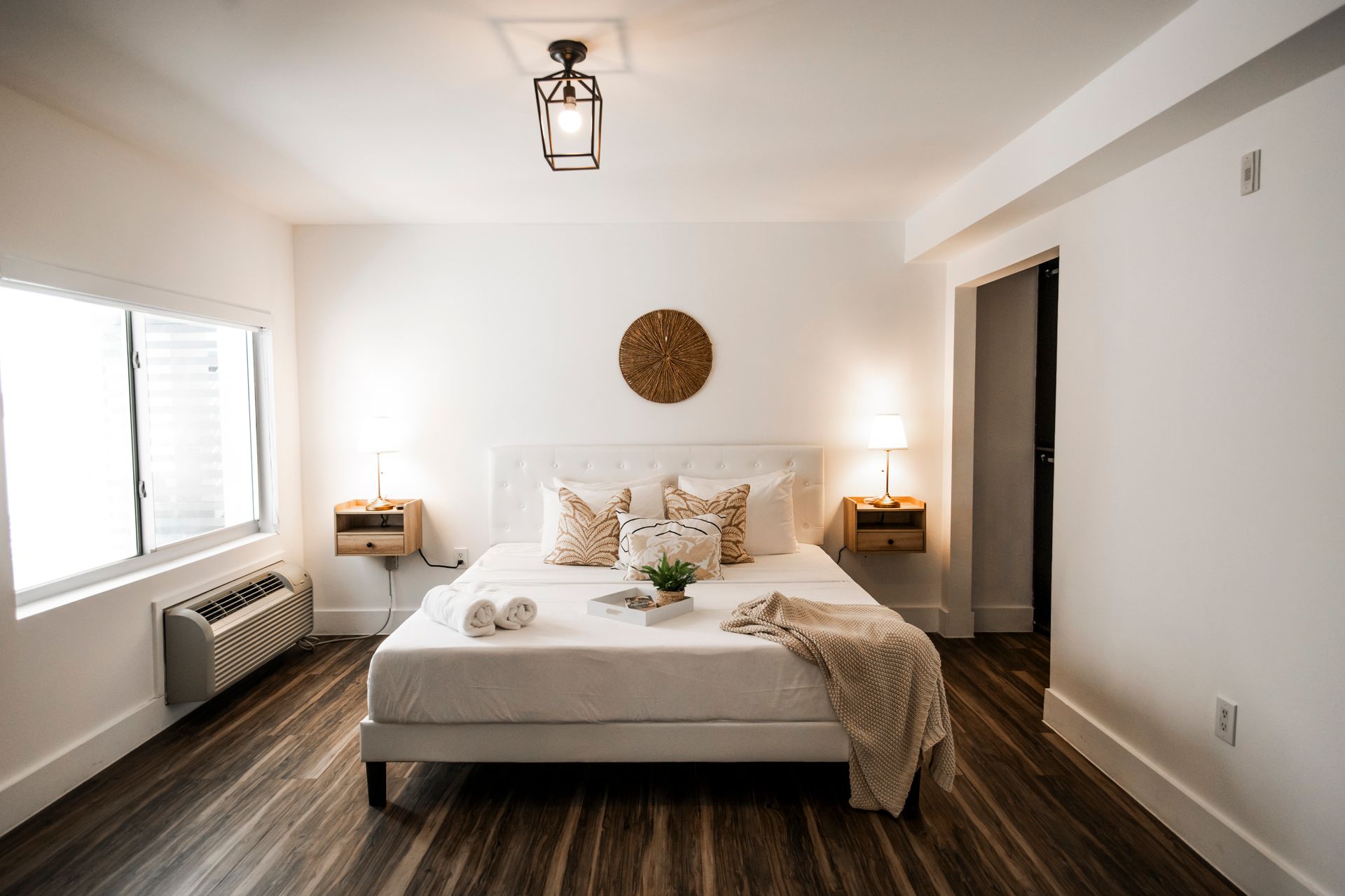 Bedroom with white walls, a bed, and wooden floors. Two bedside tables with lamps.