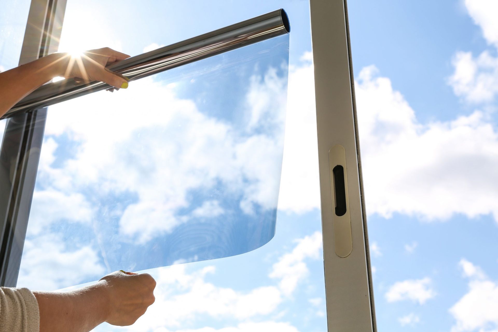 Hands opening a glass window to a bright blue sky with clouds