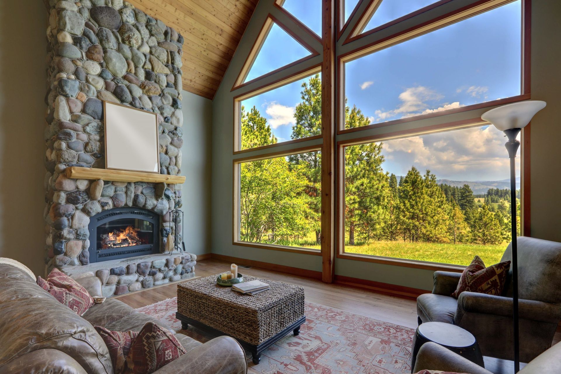 Cozy living room with stone fireplace, large windows, and a view of trees and sky.