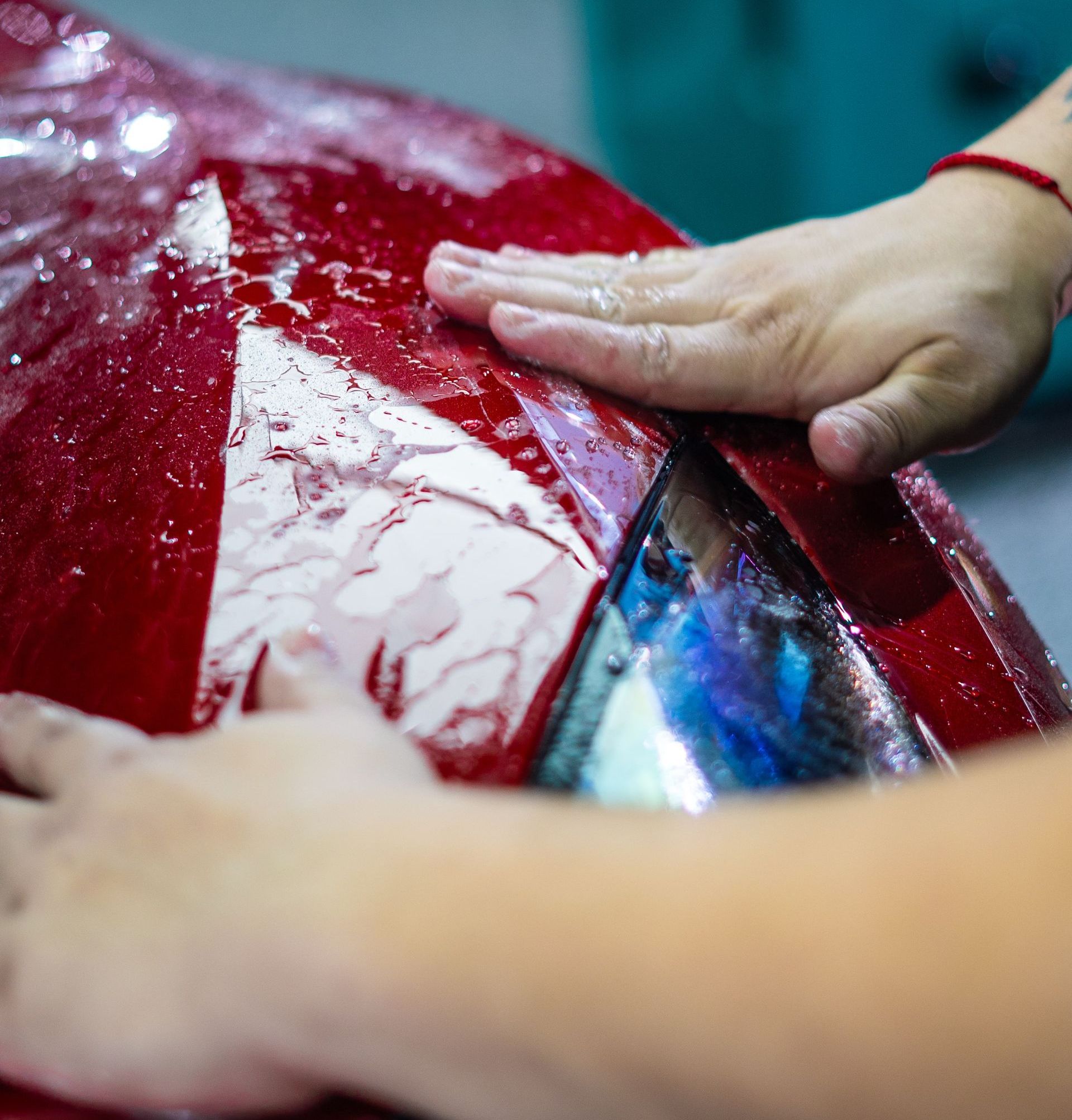 Hands polishing a wet red car body close-up