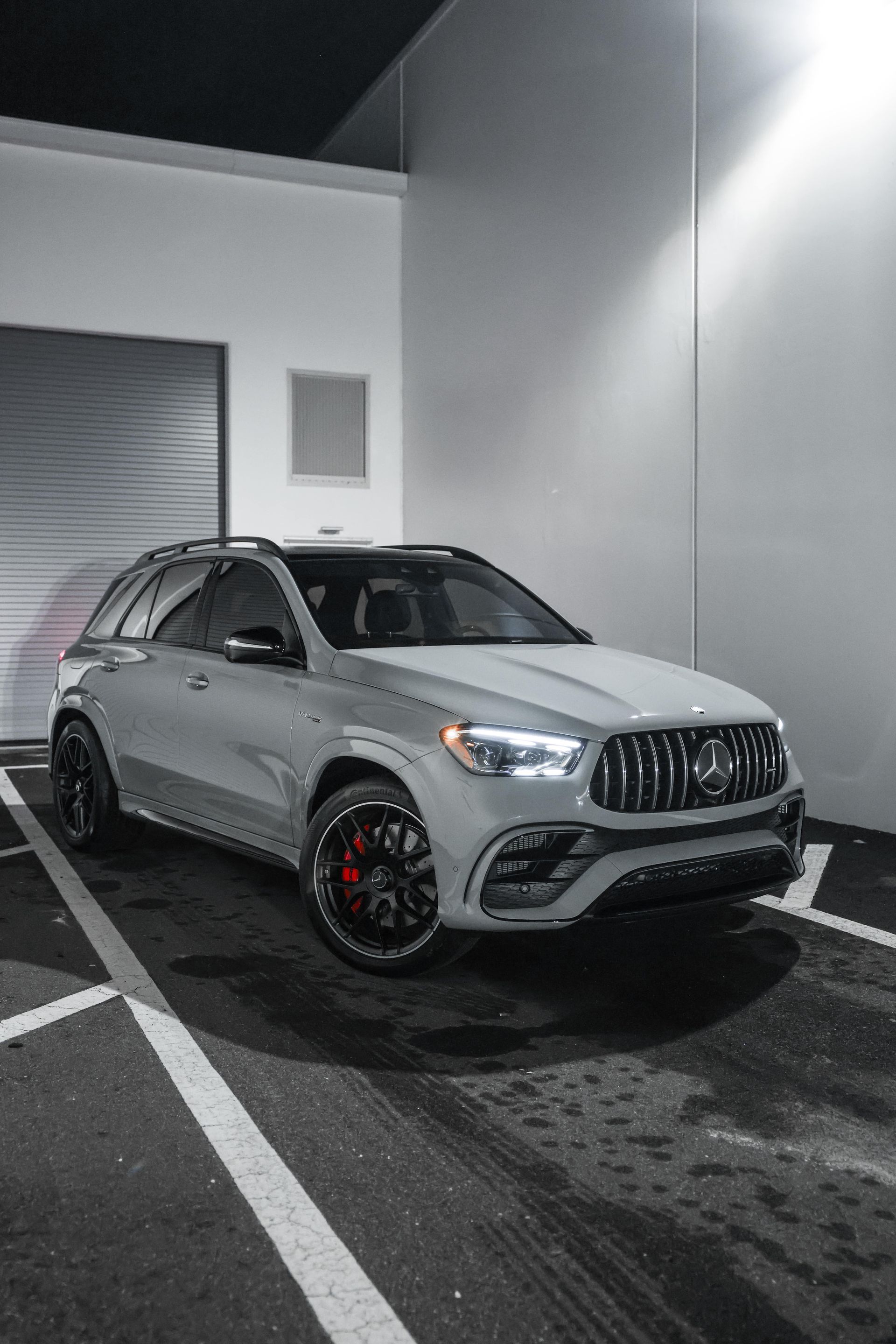 Silver Mercedes SUV parked in a wet alley beside a gray building at night