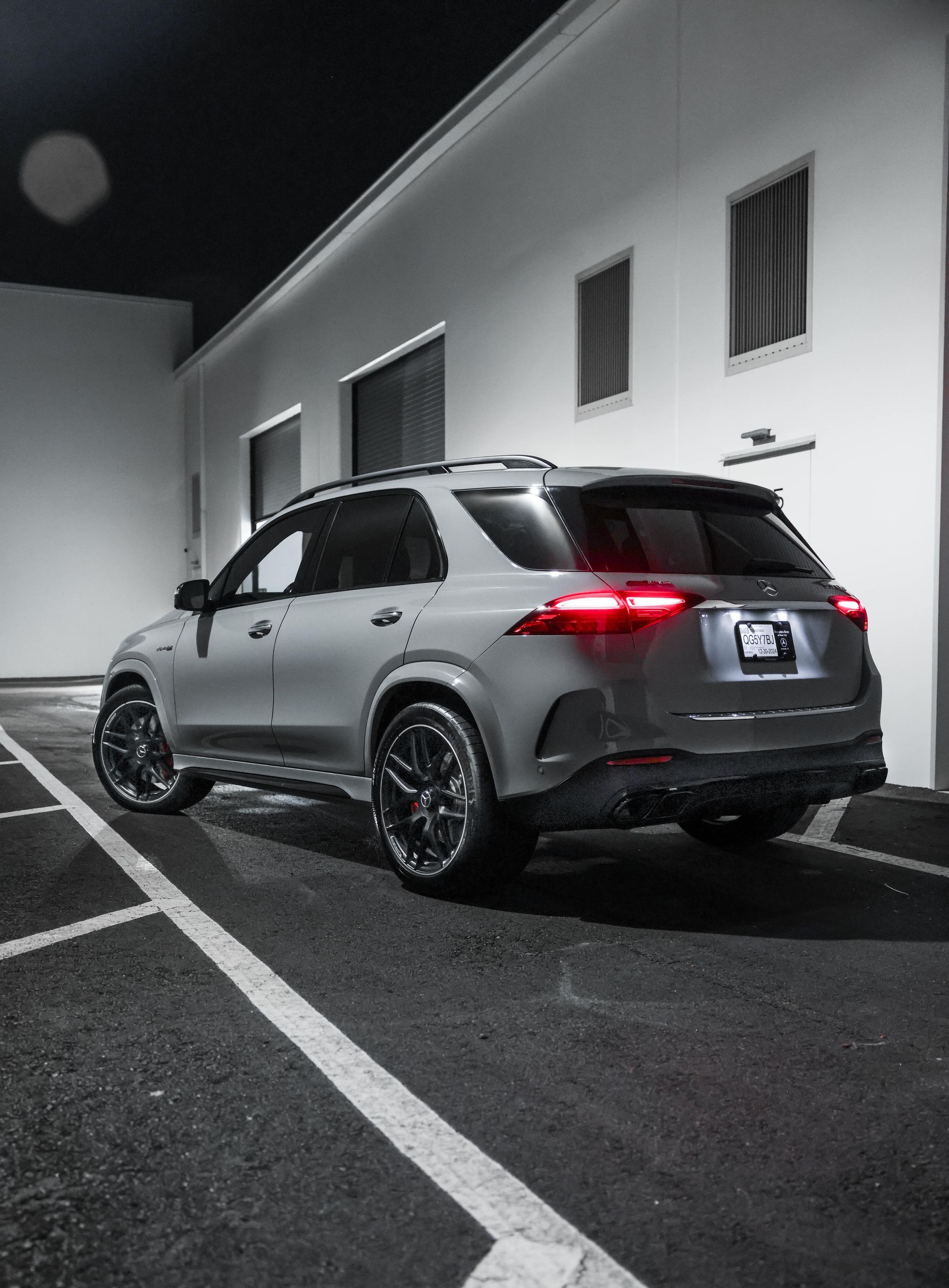 Gray SUV parked in a striped lot beside a white building at night, rear lights glowing