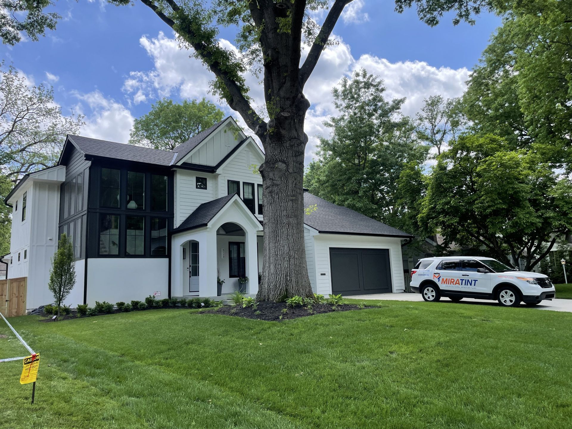 9 Benefits of Home Window Tinting White house with black accents, large tree in front. SUV in driveway with logo.