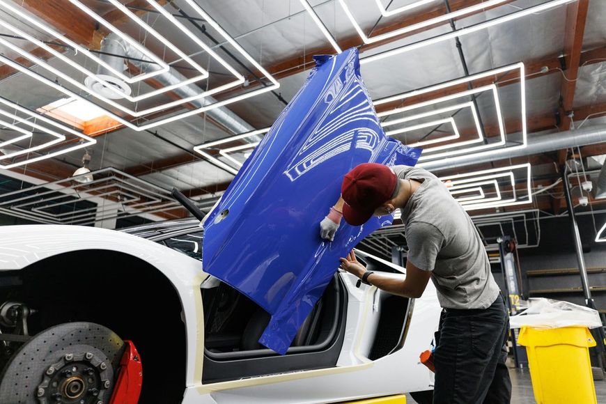 A person is polishing the hood of a blue car.