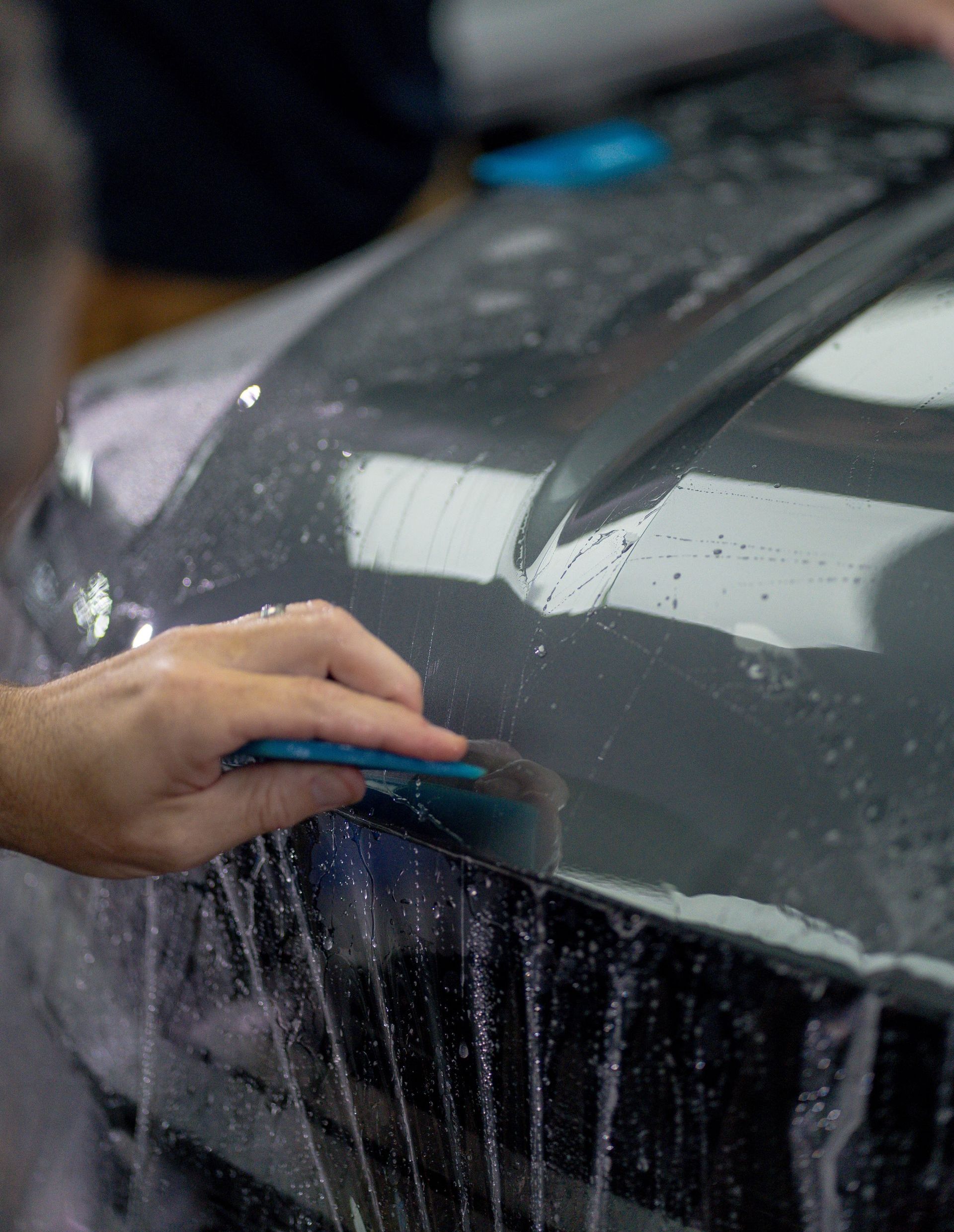 Hand washing a black car hood with soap suds and a blue sponge
