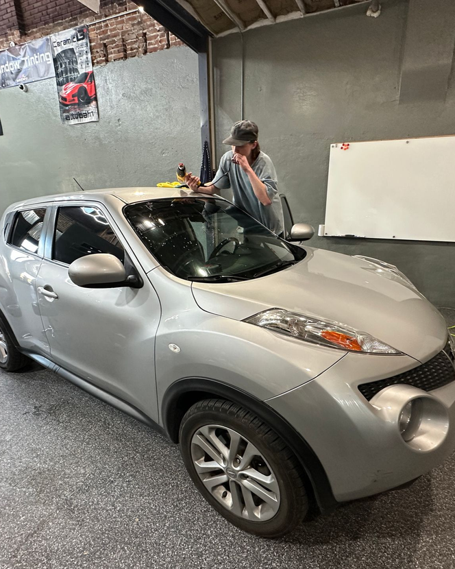 Person working on the roof of a silver Nissan Juke in a garage.