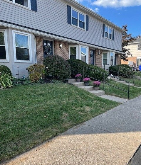 Row of beige townhouses with dark shutters and brick accents under a clear blue sky.