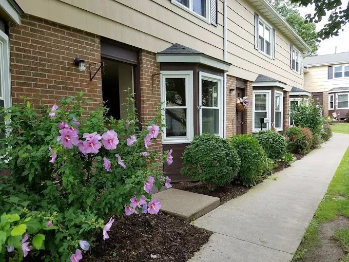 Row of townhouses with brick and siding, featuring bay windows and shrubbery.
