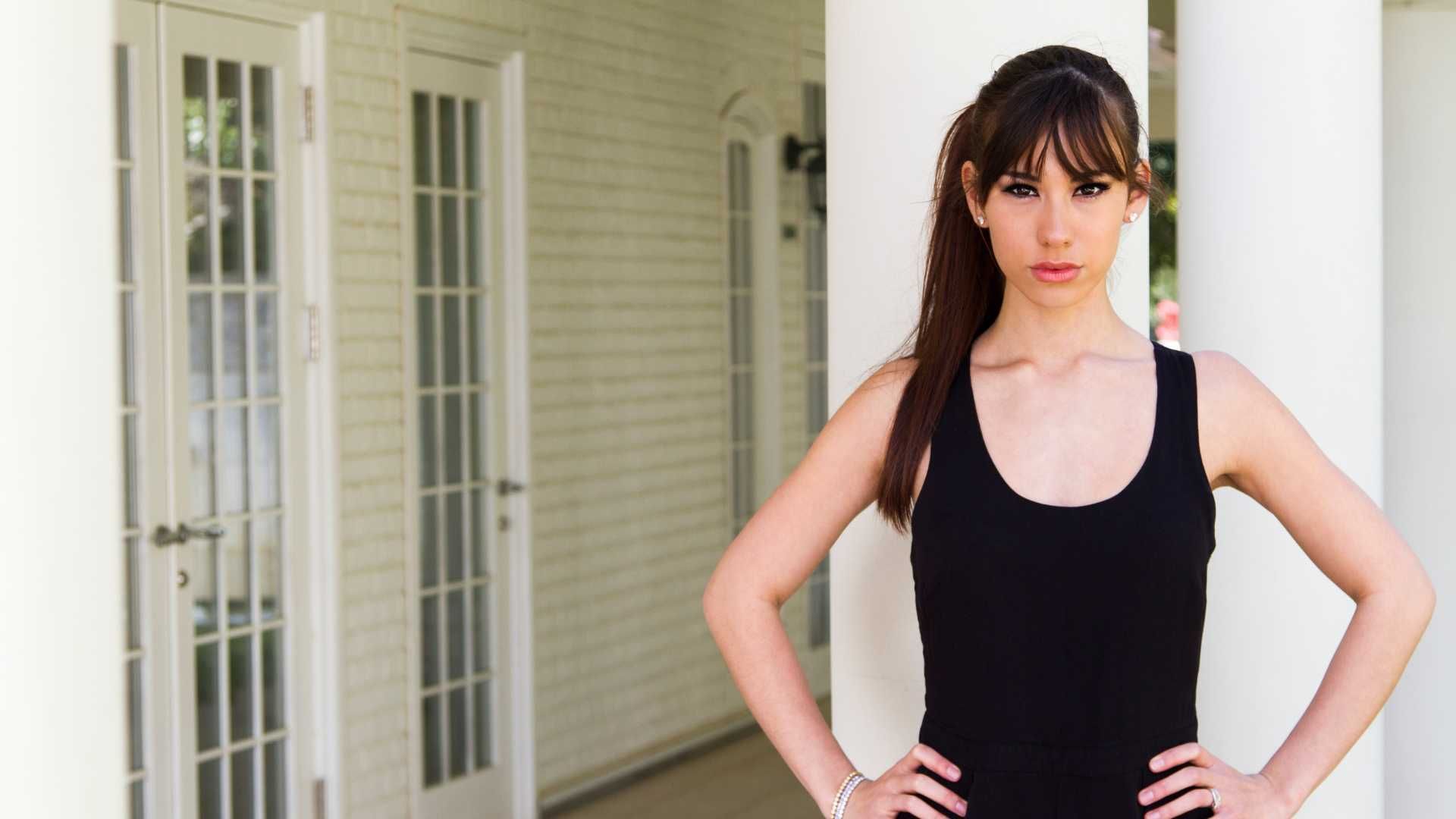 A woman in a black tank top is standing with her hands on her hips.