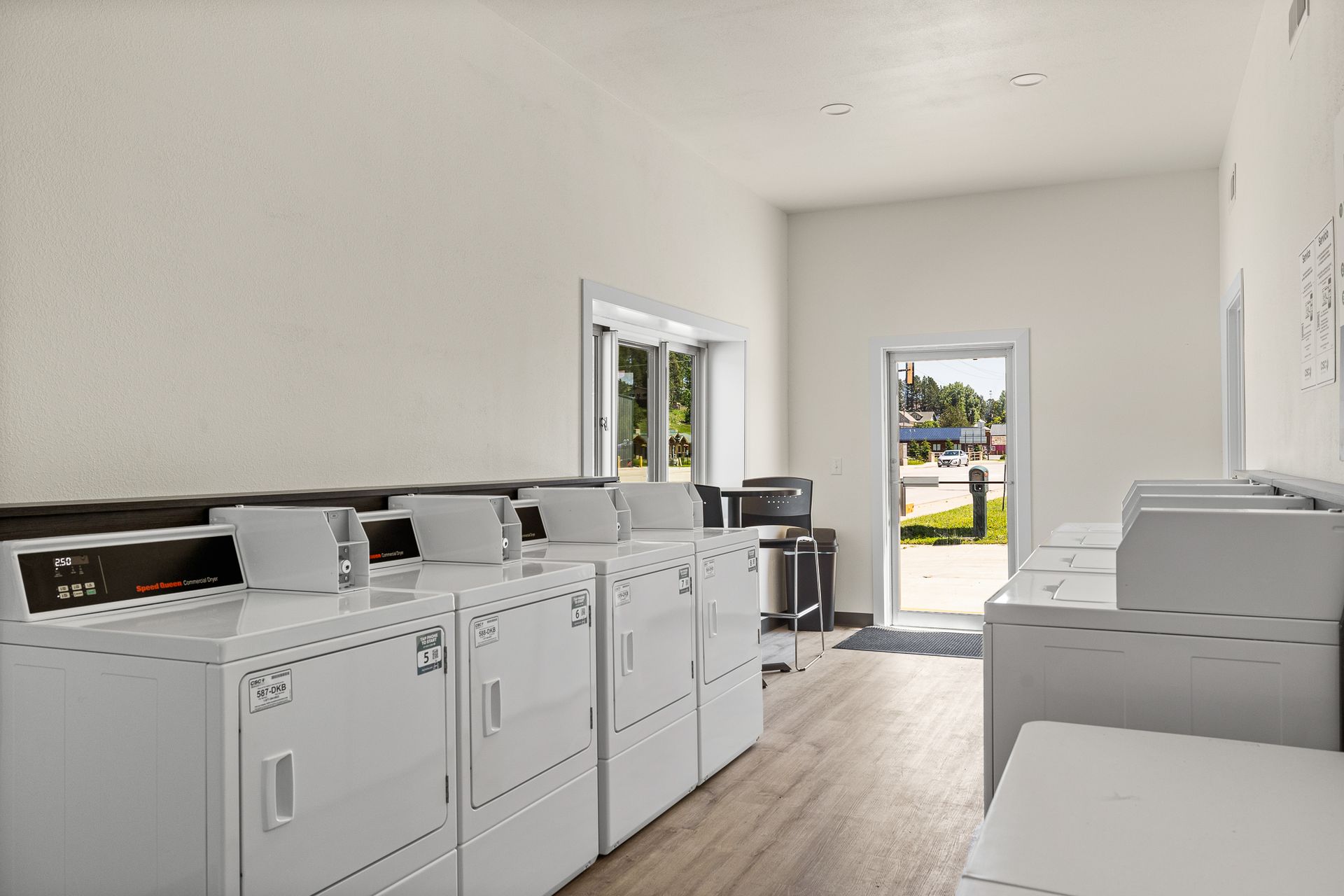 Bright laundry room with rows of white washers and dryers and an open door to the outside.