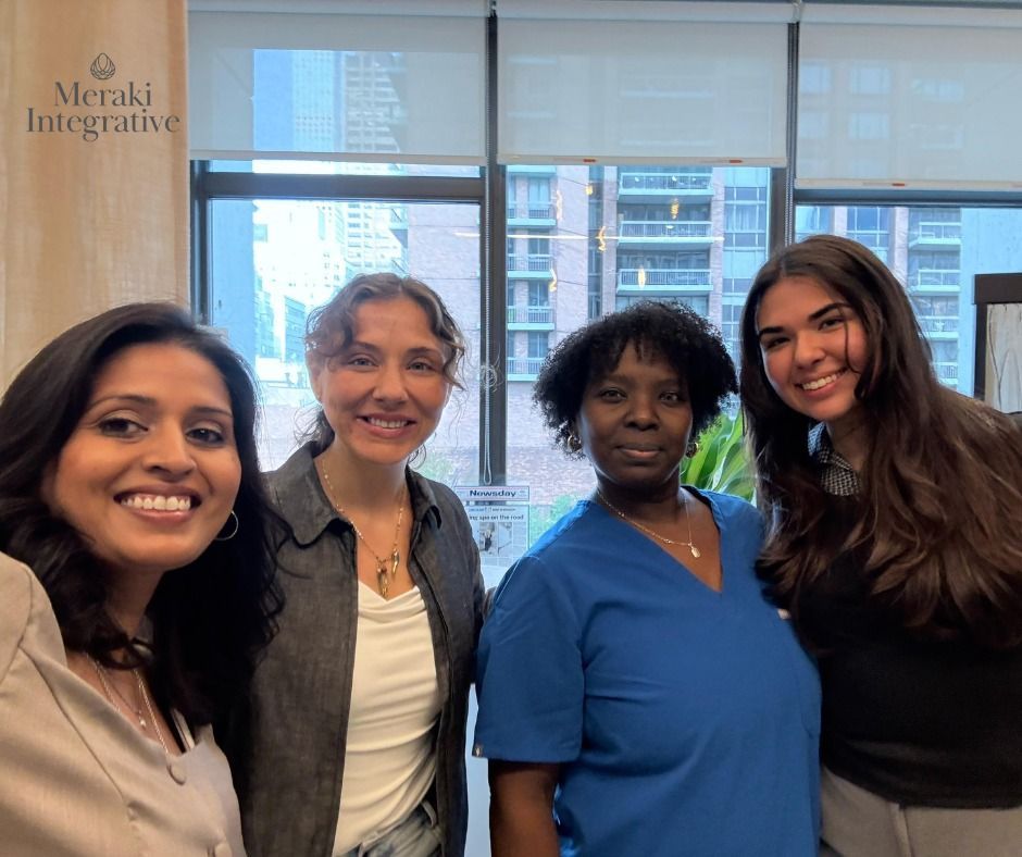 Four smiling people pose indoors; windows and a city view are in the background.