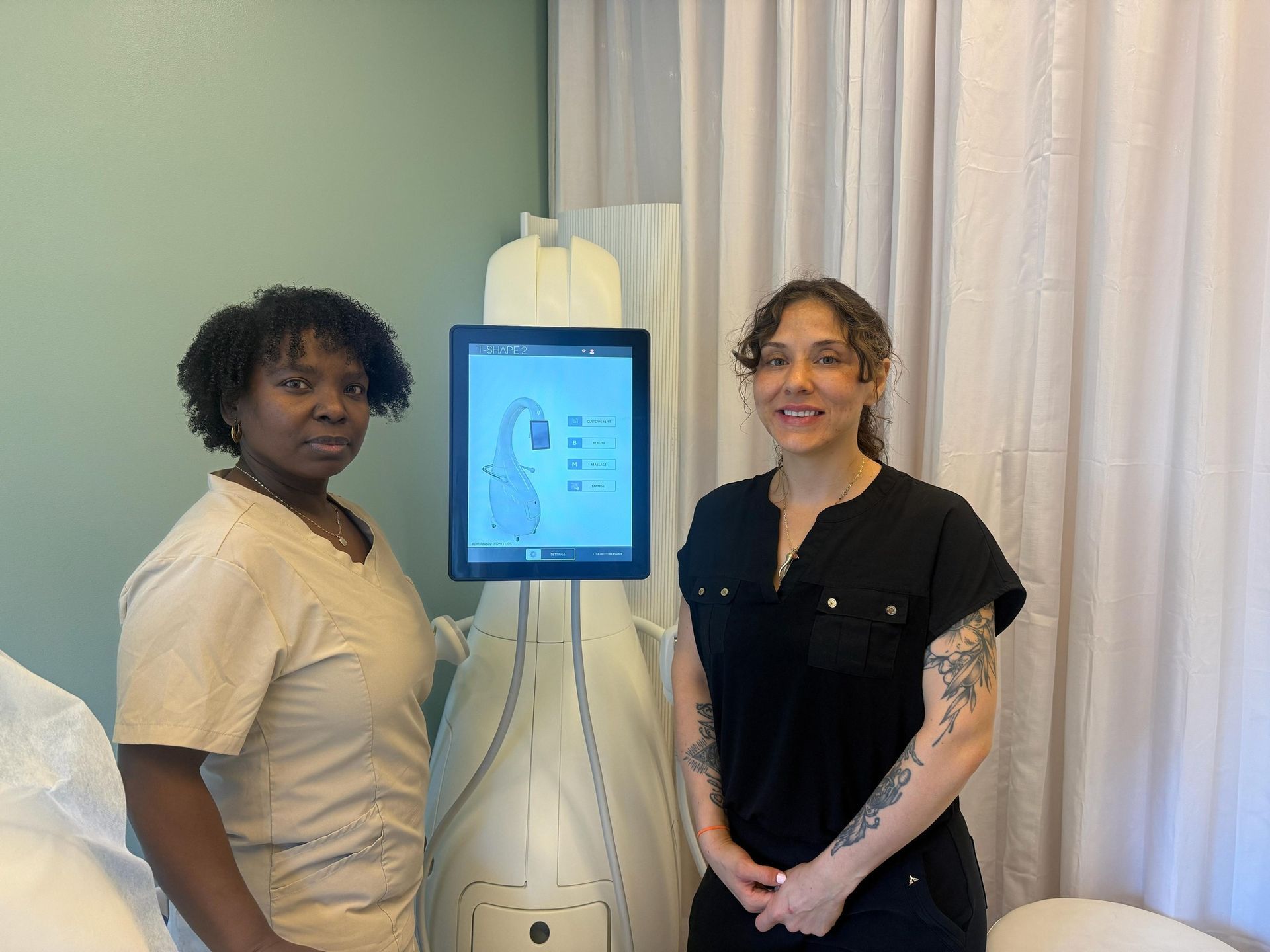 Two people standing near a medical device. One person in tan scrubs and the other in a black top.