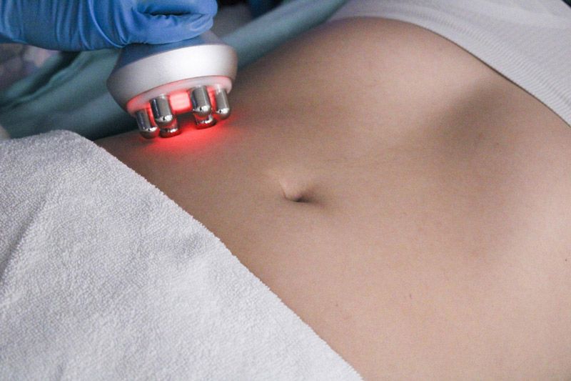 A device with red lights is held on a person's abdomen, partially covered by a white towel.