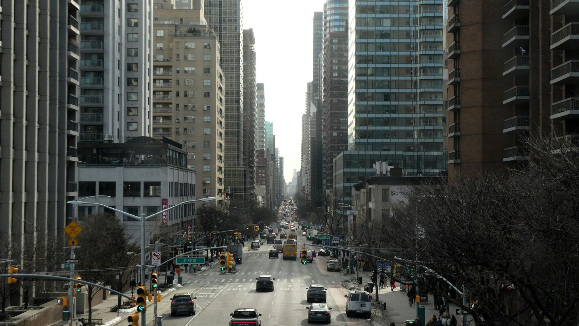 A city street view looking down an avenue lined with high-rise buildings and moderate traffic.