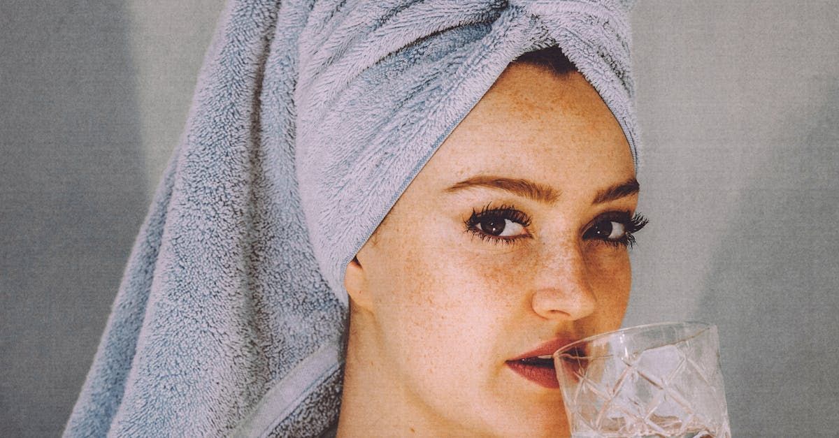 A woman with a towel wrapped around her head is drinking from a glass.