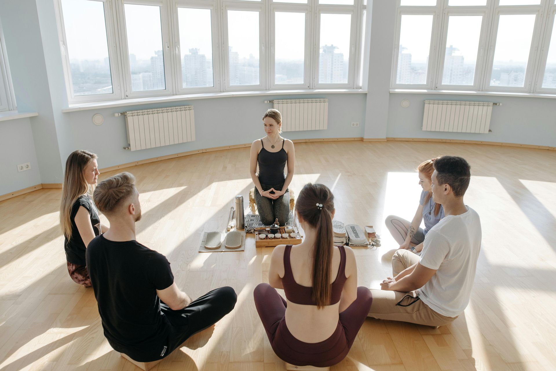 People sitting in a circle on yoga mats in a bright studio during a meditation session