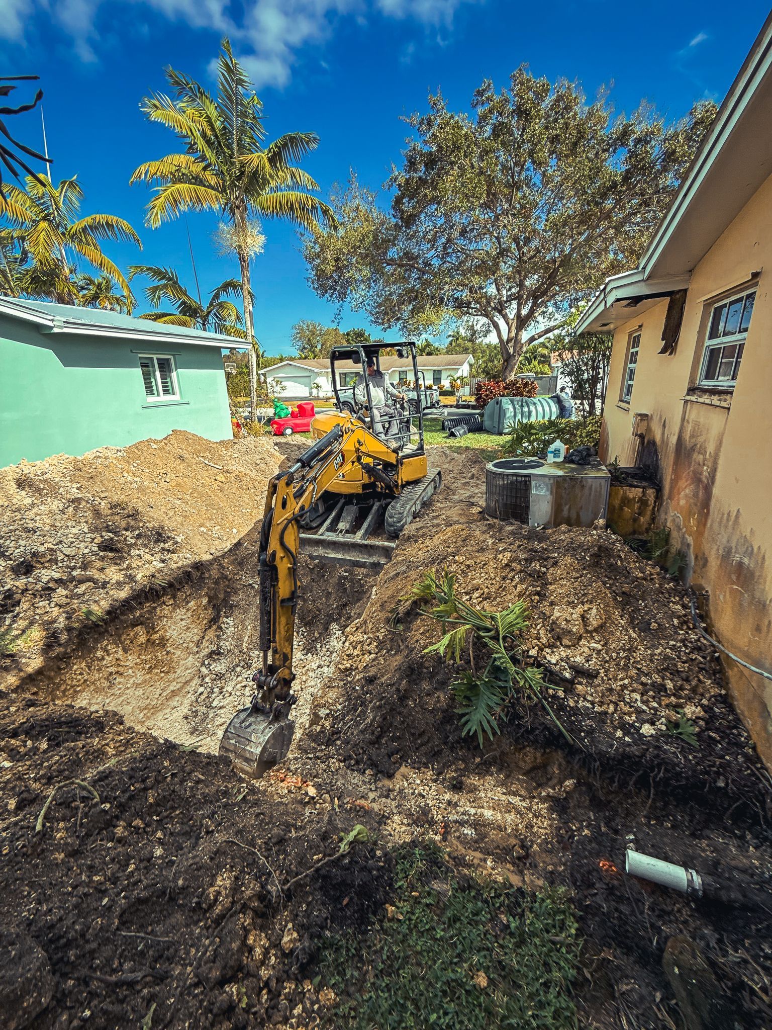 A yellow excavator is digging a hole in front of a house.