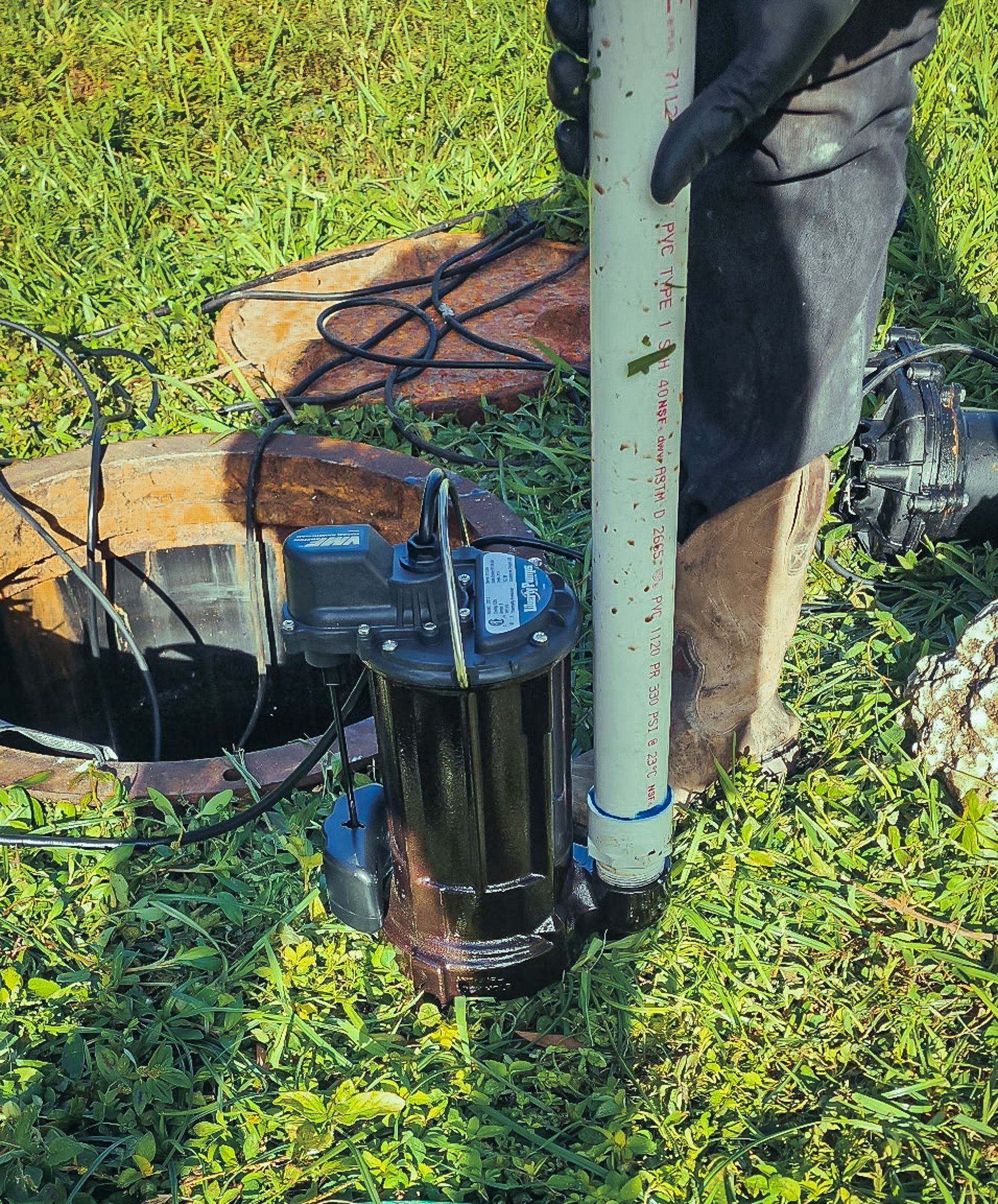 A person is cleaning a drain with a pump in the grass.