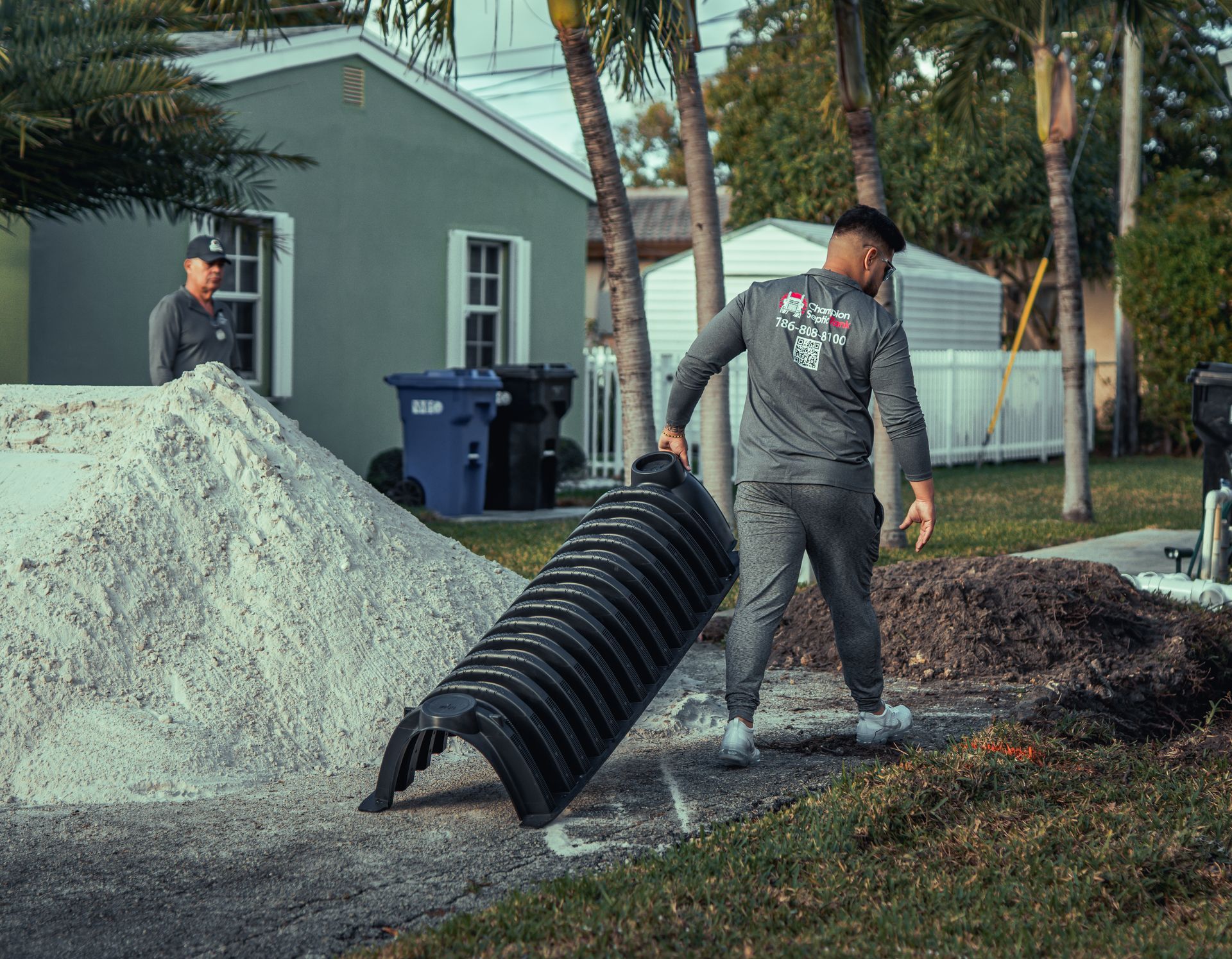 A man is carrying a large pipe in a yard.