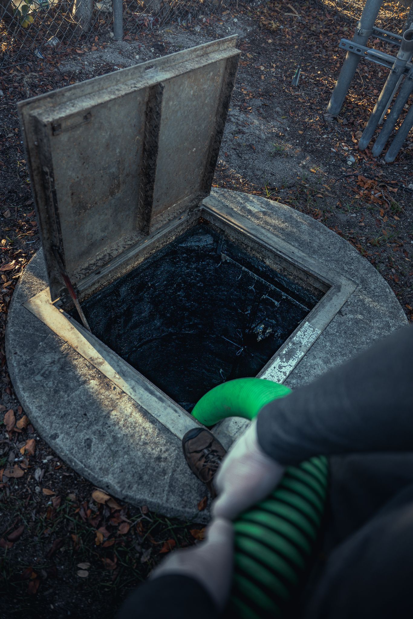 A person is pumping water into a septic tank with a green hose.
