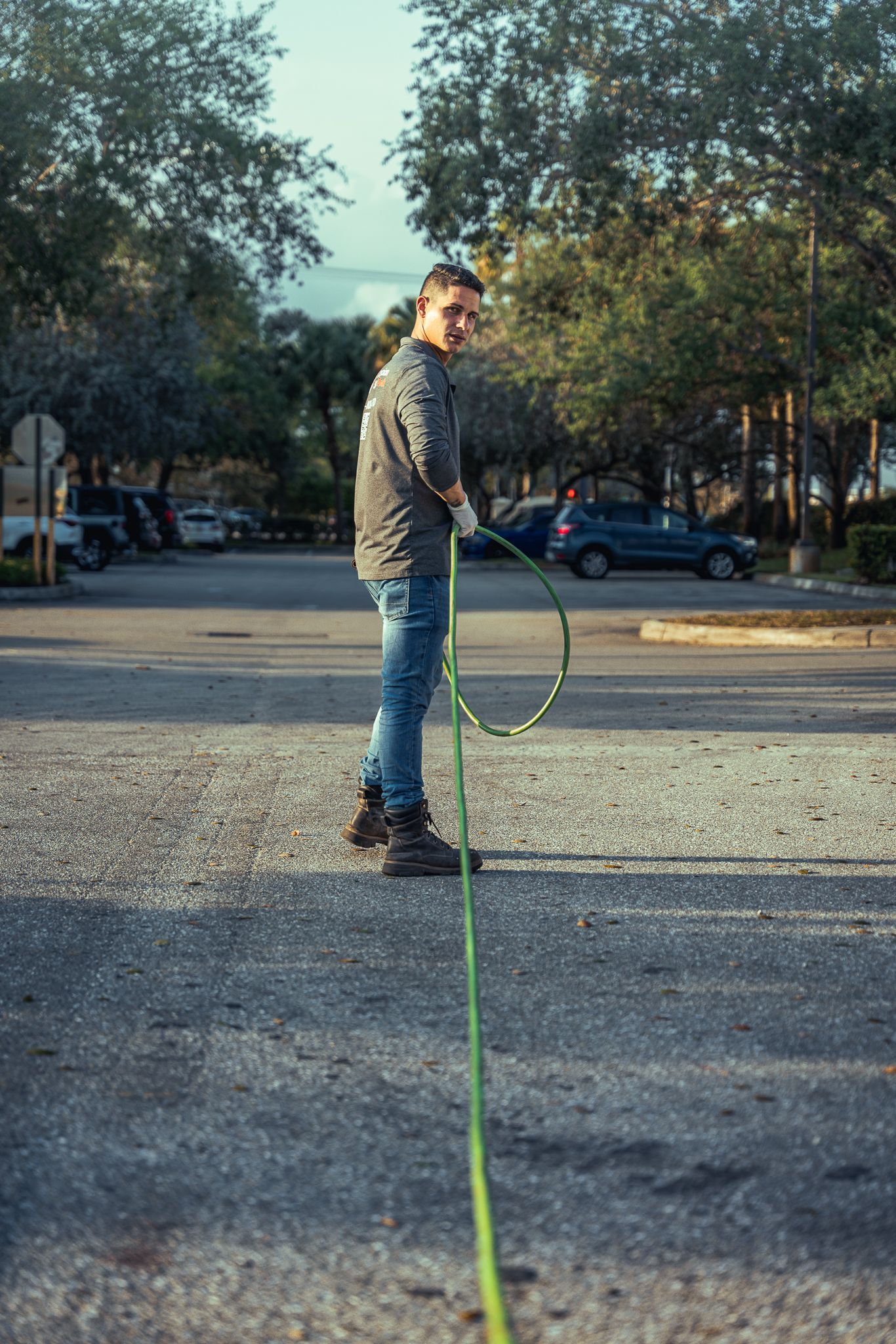 A man is standing next to a green hose in a parking lot.