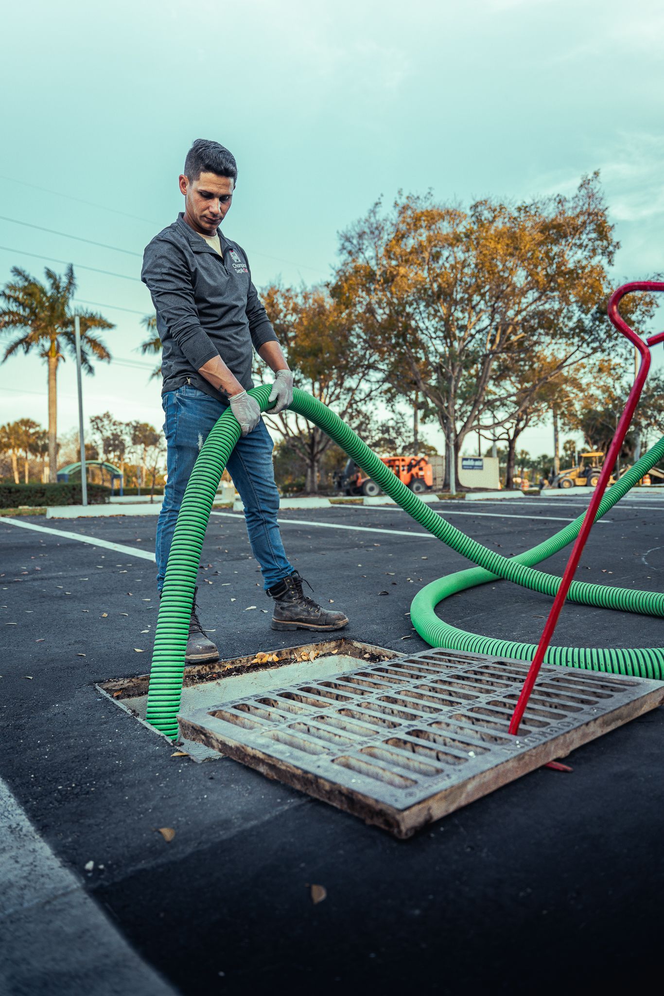 A man is pumping water into a manhole cover with a green hose.