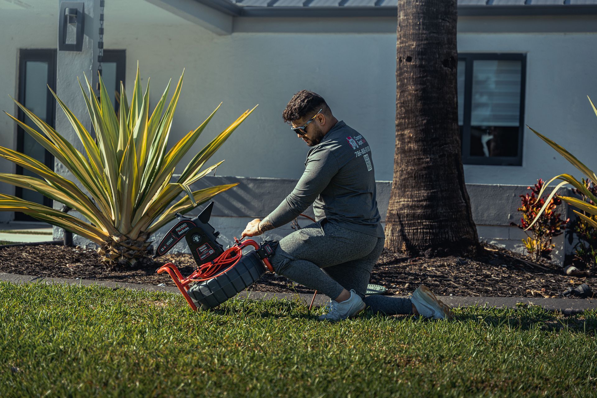 A man is kneeling down in the grass while using a lawn mower.